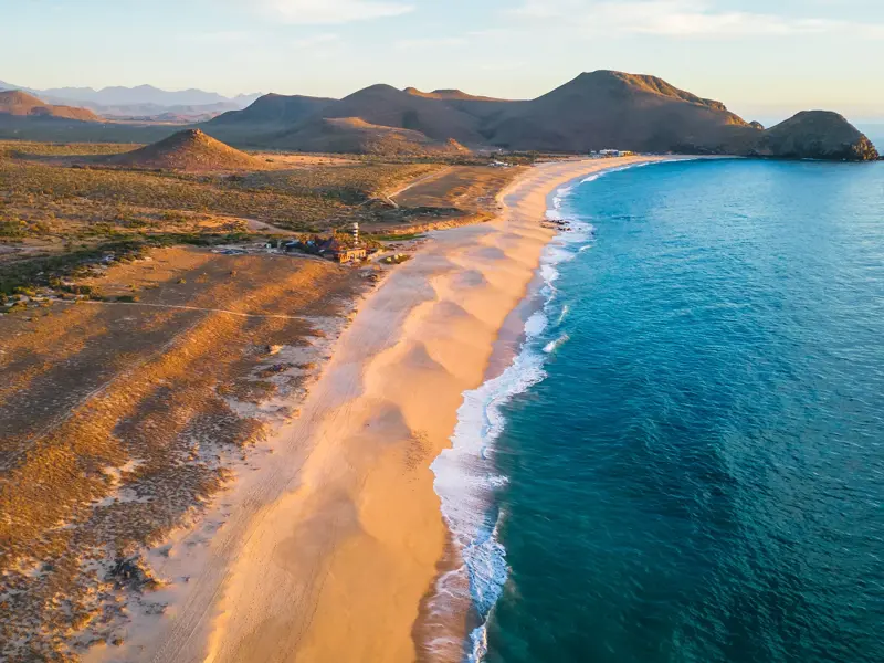 Goldener Sandstrand an der Küste von Baja California, umspült von türkisfarbenem Pazifik vor einer kargen Berglandschaft.