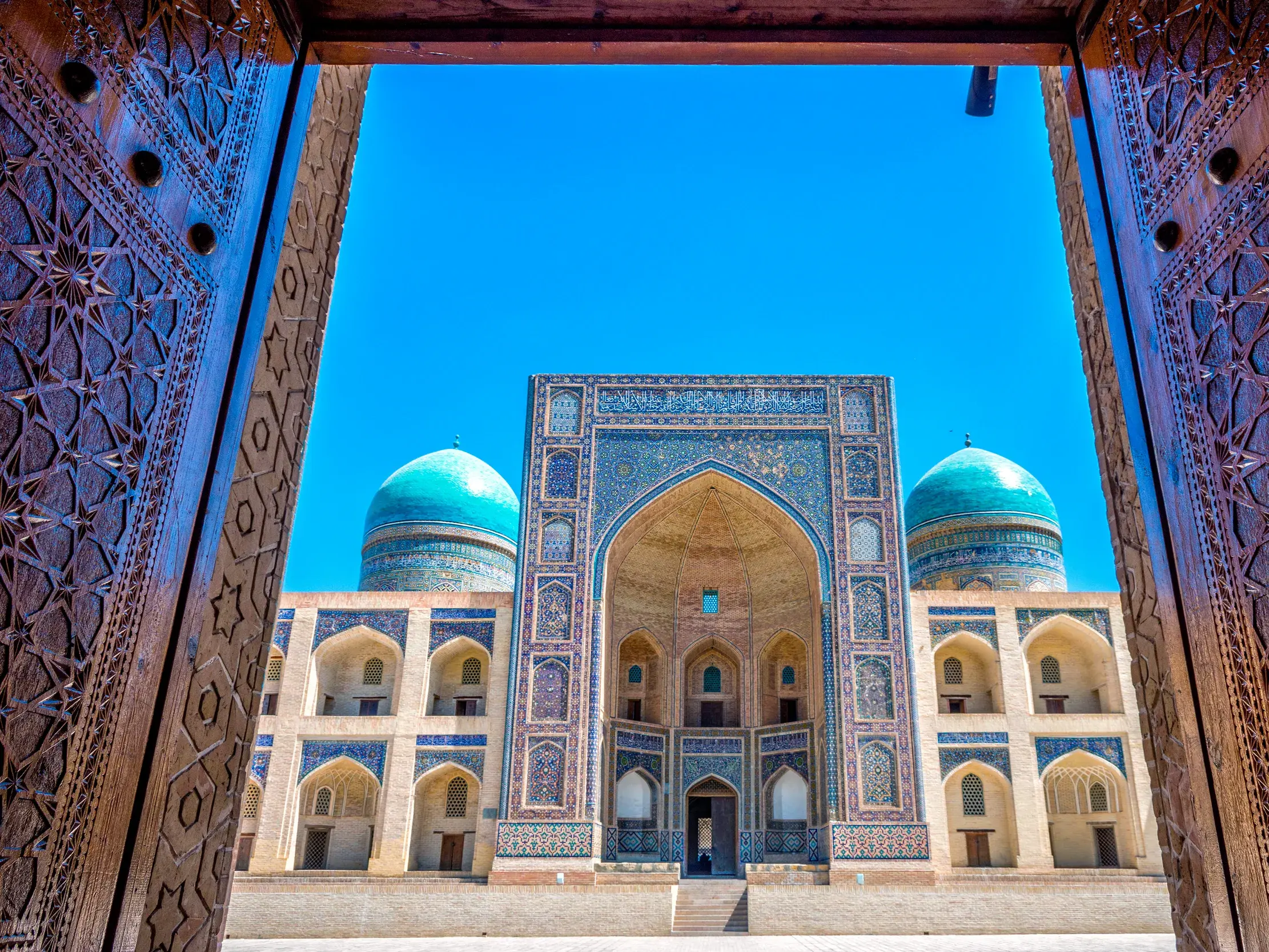 Geöffnete, reich verzierte Holztore geben den Blick frei auf die prachtvolle Mir-i-Arab-Medrese in Buchara, Usbekistan.