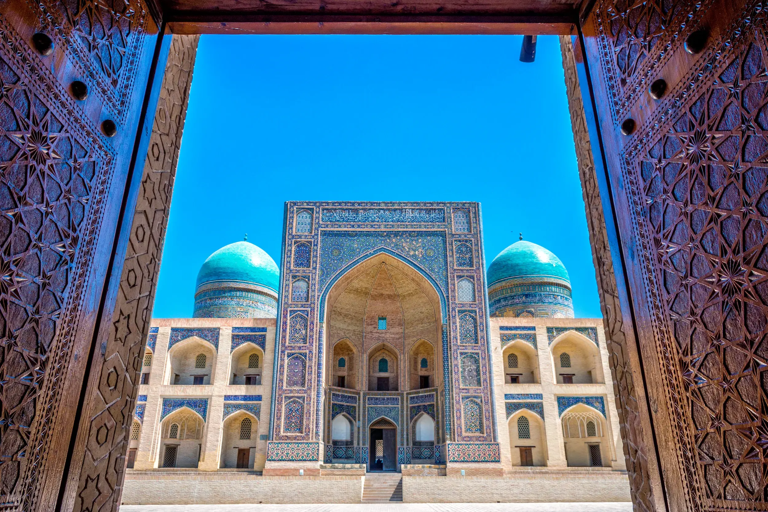 Geöffnete, reich verzierte Holztore geben den Blick frei auf die prachtvolle Mir-i-Arab-Medrese in Buchara, Usbekistan.