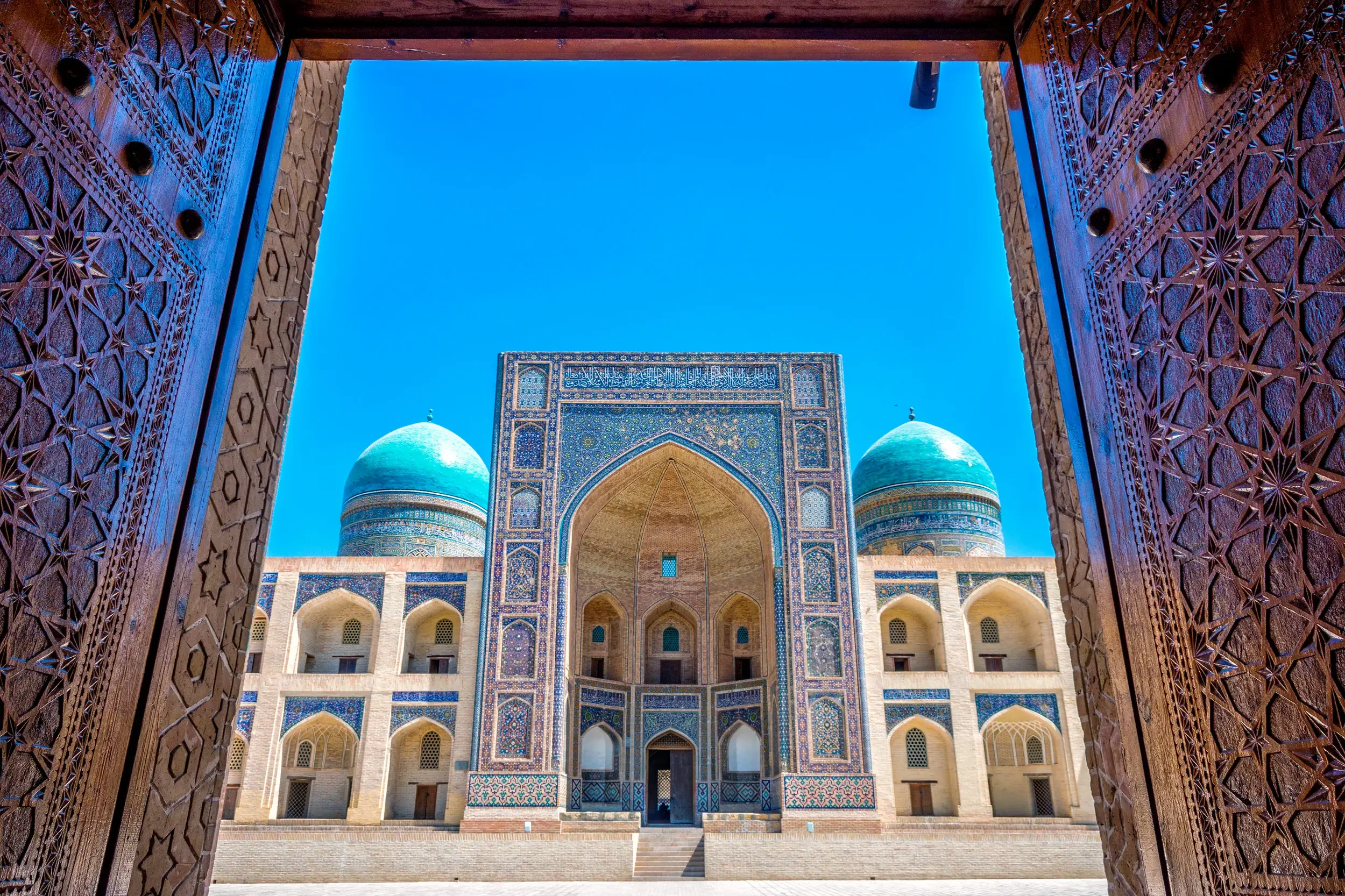 Geöffnete, reich verzierte Holztore geben den Blick frei auf die prachtvolle Mir-i-Arab-Medrese in Buchara, Usbekistan.