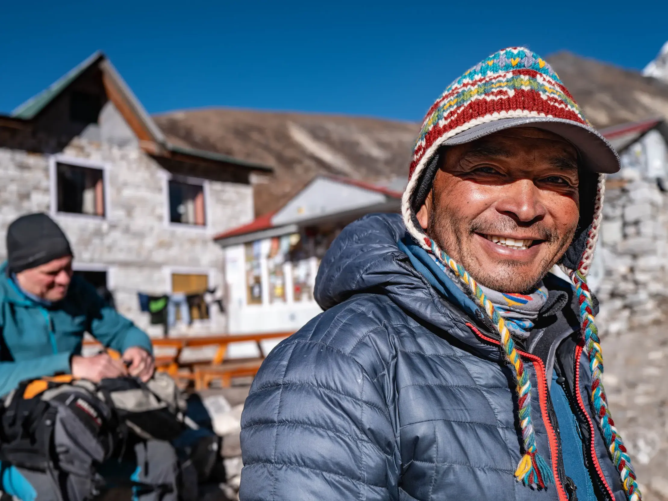 Ein nepalesischer Bergführer mit bunter Mütze lächelt herzlich während einer Trekking-Pause in der Dolpo-Region, Nepal.