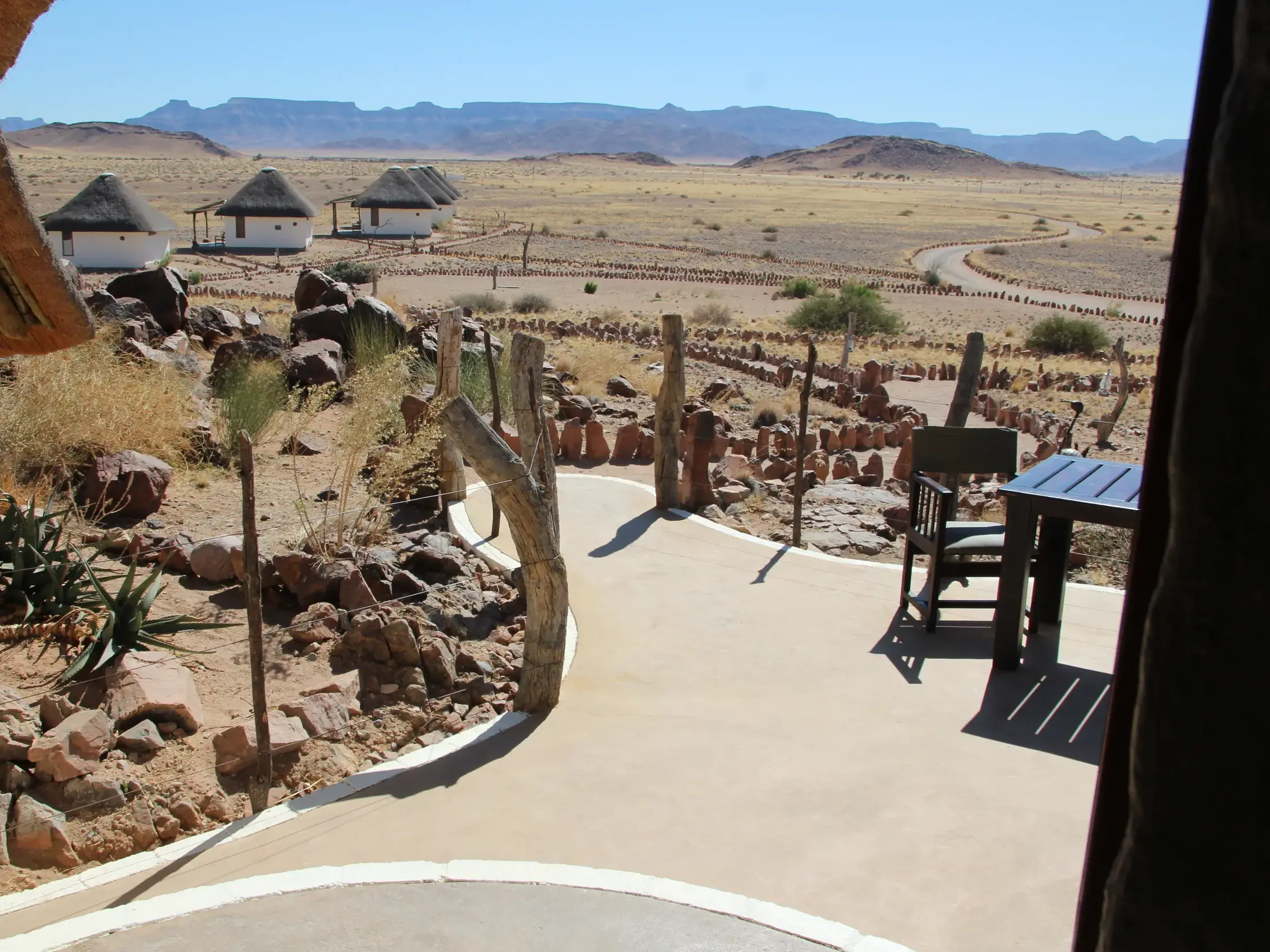Blick von der Terrasse einer Lodge auf Bungalows in der weiten, felsigen Landschaft des Erongo-Gebirges in Namibia.