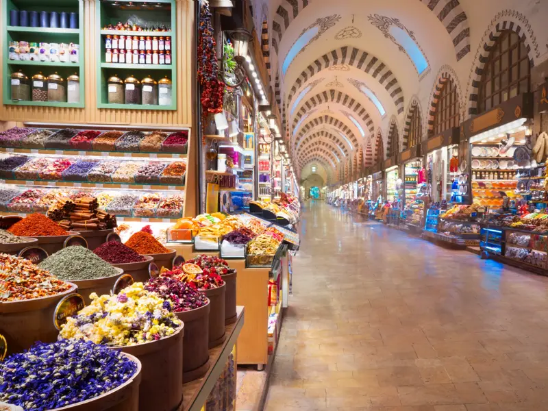 Farbenfrohe Gewürze und Tees an einem Marktstand im langen, gewölbten Gang des historischen Gewürzbasars in Istanbul.