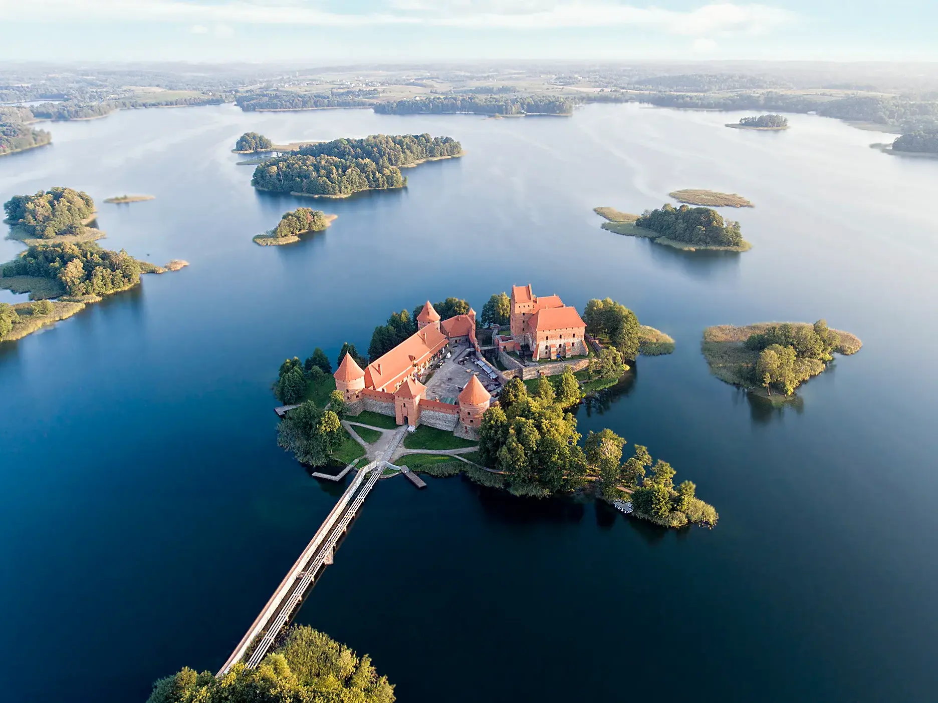 Die gotische Wasserburg Trakai in Litauen aus der Vogelperspektive, umgeben von kleinen Inseln in einer weiten Seenlandschaft.