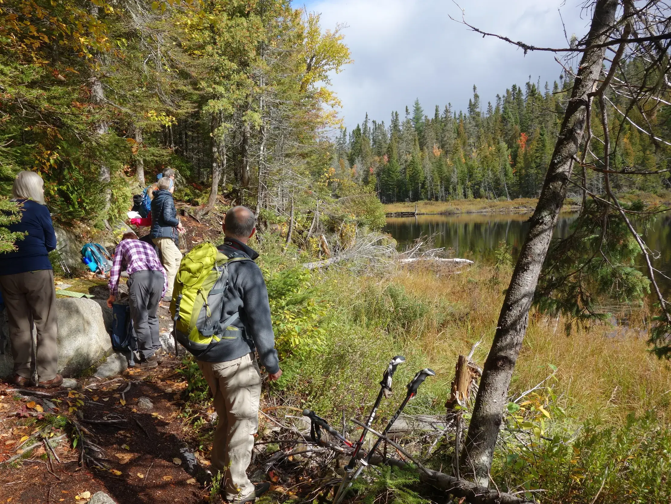 Eine kleine Reisegruppe mit Rucksäcken wandert auf einem Pfad entlang eines Sees durch den herbstlichen Wald in Québec, Kanada.