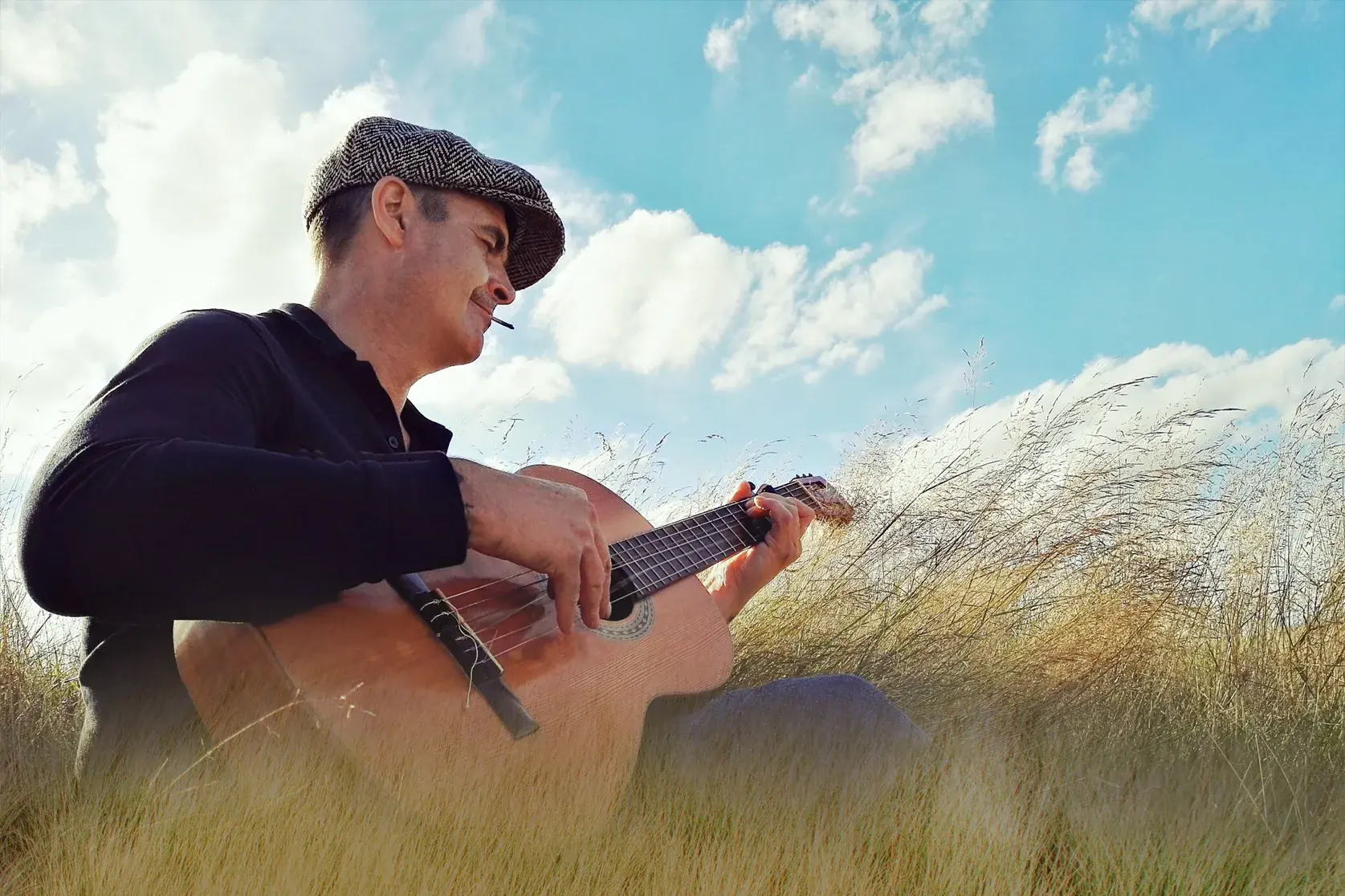 Ein Musiker mit Schiebermütze spielt auf seiner Gitarre melancholische Lieder in der weiten, grasbewachsenen Landschaft Irlands.