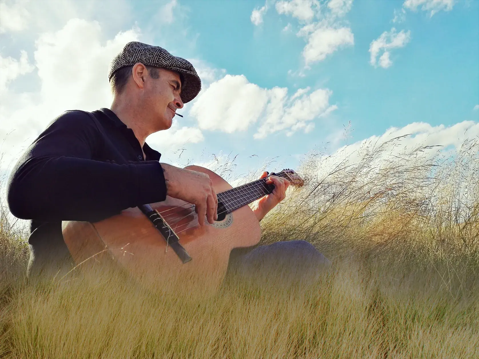 Ein Musiker mit Schiebermütze spielt auf seiner Gitarre melancholische Lieder in der weiten, grasbewachsenen Landschaft Irlands.