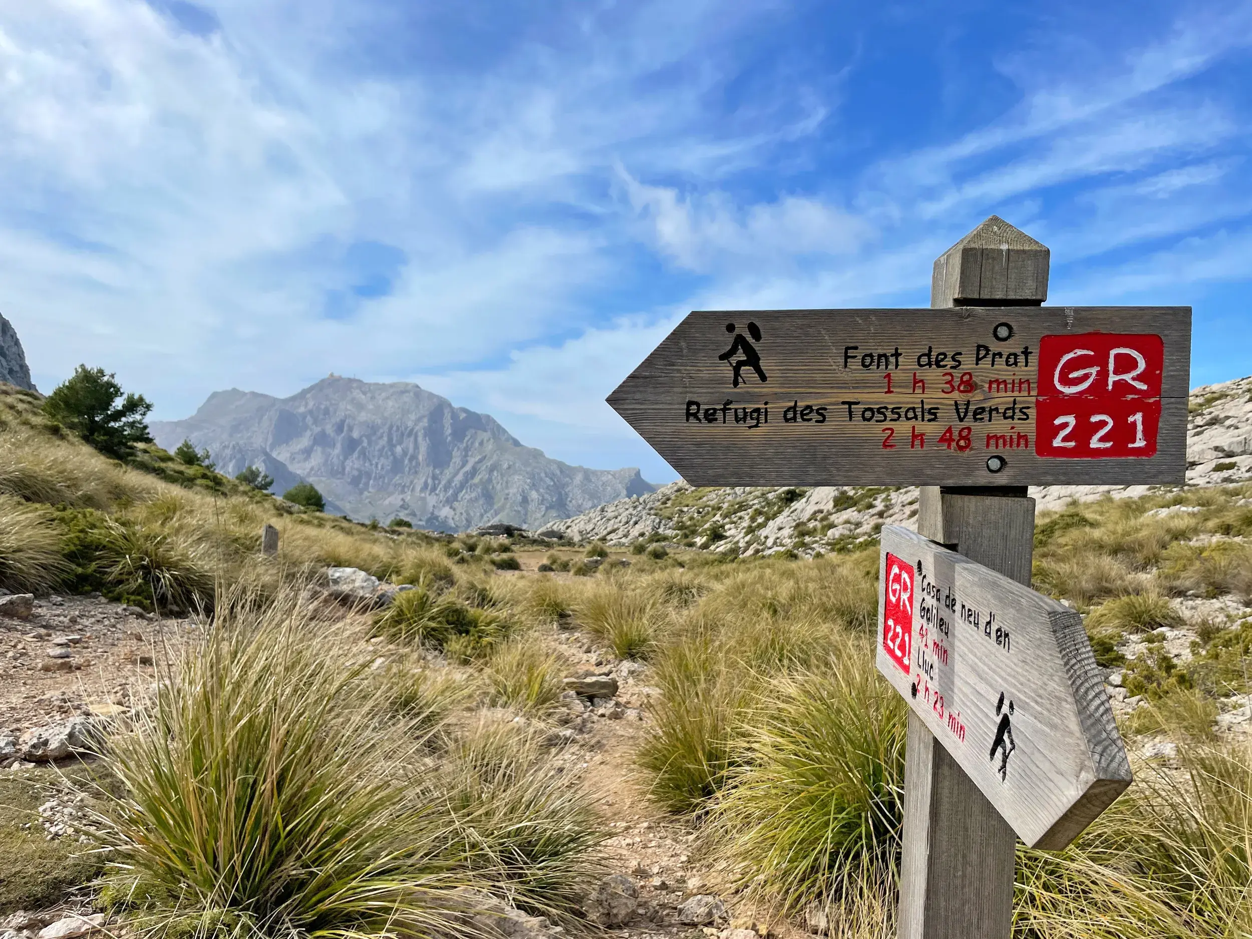 Ein Wegweiser am Fernwanderweg GR 221 weist den Weg durch die sonnige Berglandschaft der Serra de Tramuntana auf Mallorca.