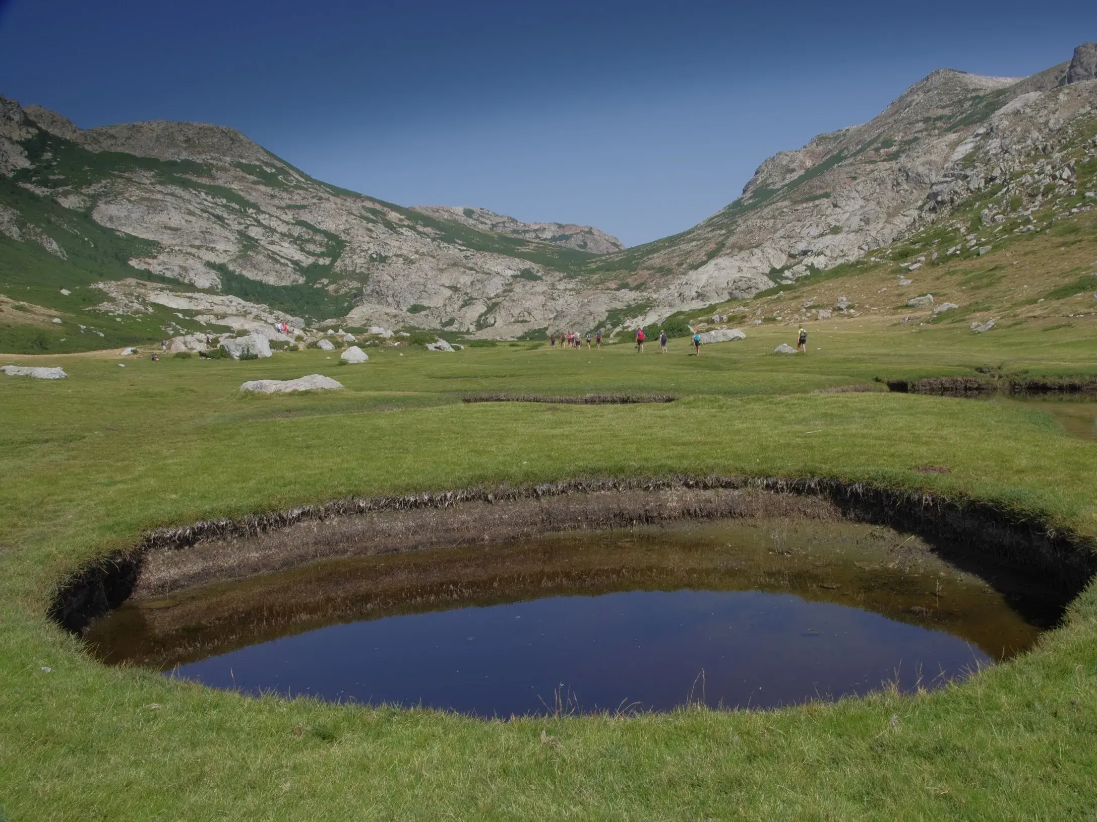 Eine Gruppe wandert beim Trekking auf dem GR20 über die Hochebene Cuscione mit ihren typischen Pozzine-Wasserlöchern.
