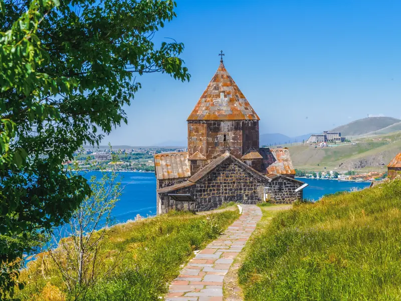 Gepflasterter Weg zum historischen Kloster Sewanawank auf einer Anhöhe mit Blick auf den tiefblauen Sewansee in Armenien.