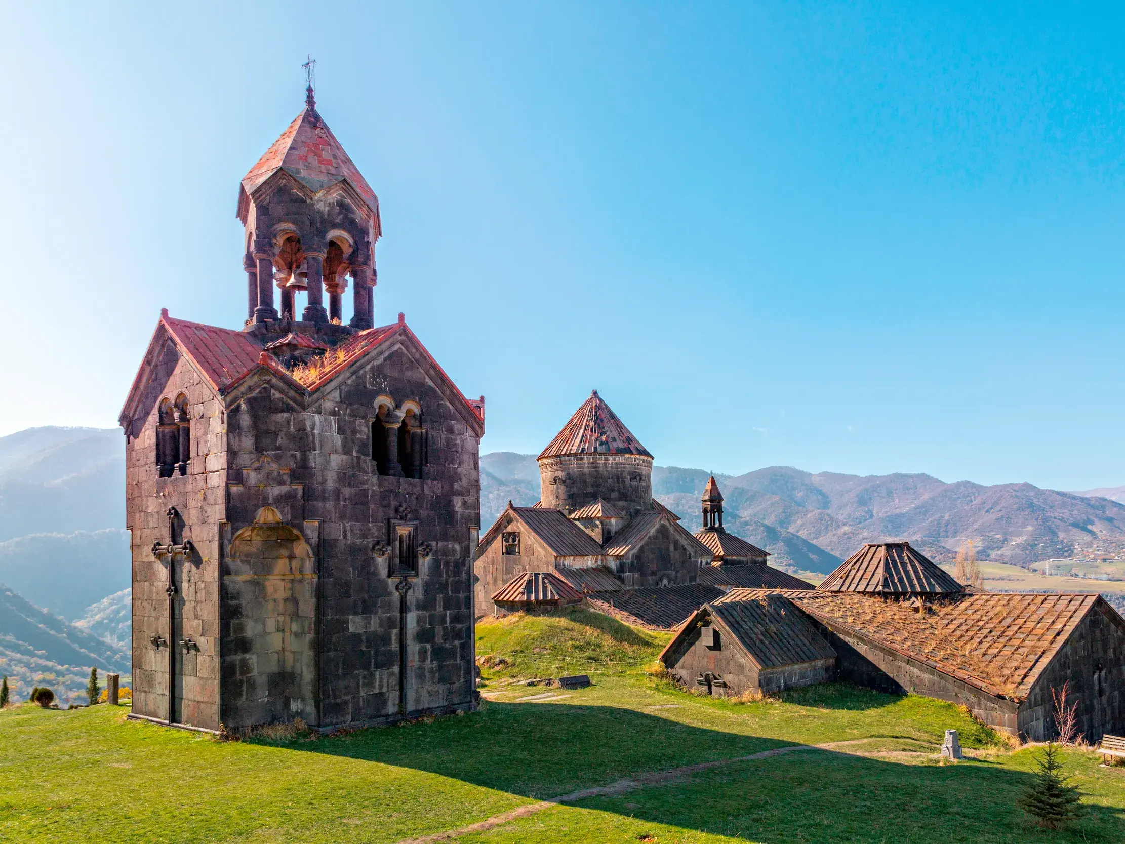 Das steinerne Kloster Haghpat in Armenien mit Glockenturm, gelegen auf einer Wiese vor der Bergkulisse des Kleinen Kaukasus.