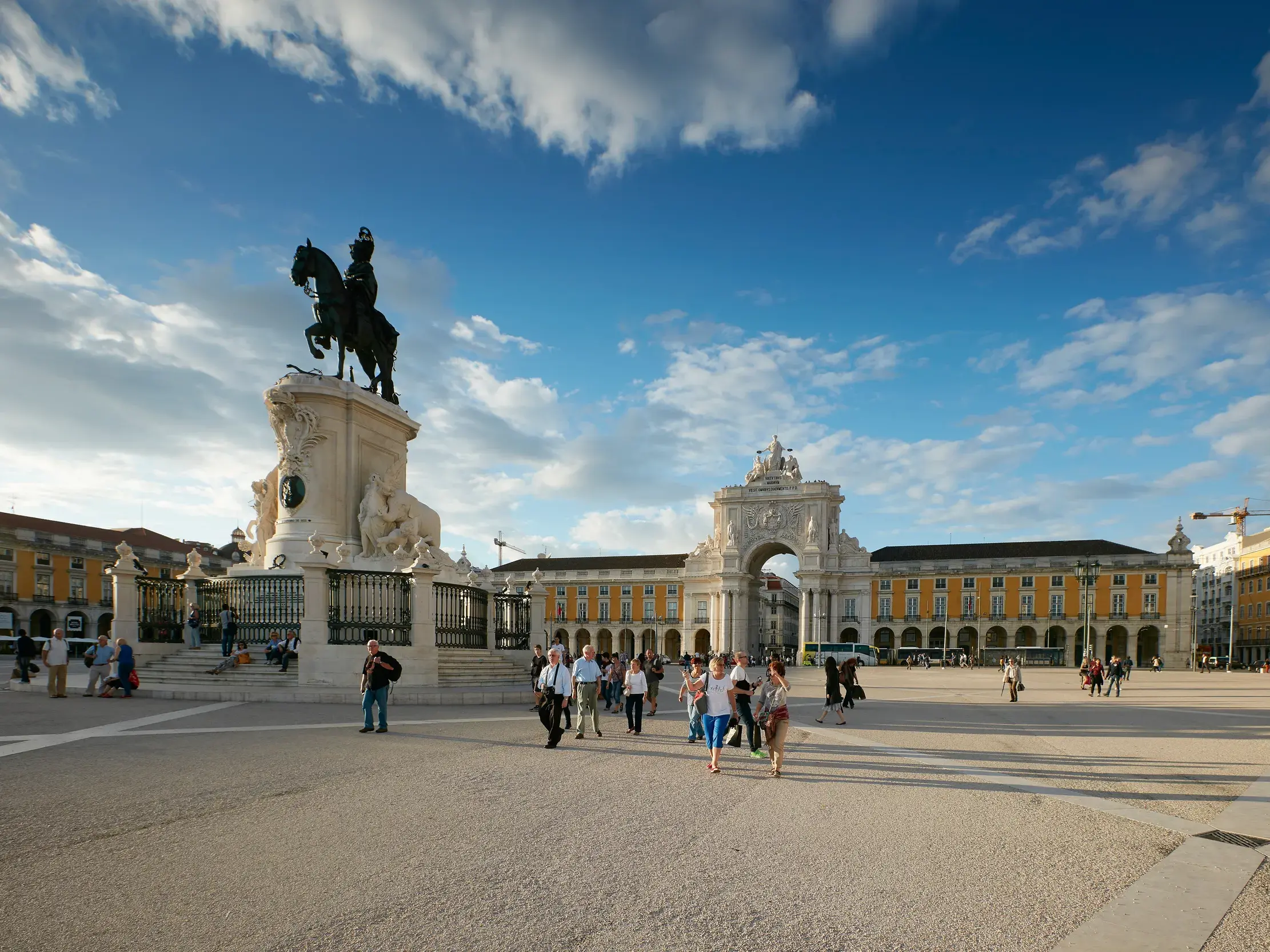 Monumentales Reiterstandbild und Triumphbogen auf einem weiten Platz in Lissabon, auf dem Besucher bei Sonnenschein flanieren.