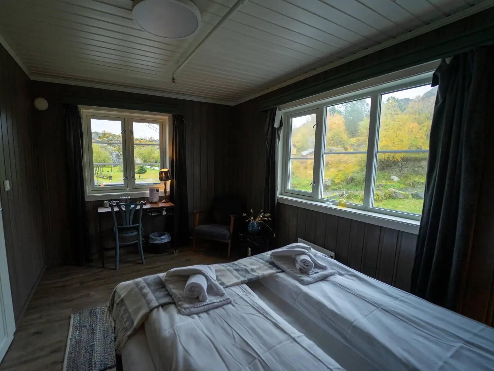 Gemütliches Hotelzimmer auf den Lofoten mit gemachtem Bett und Blick durch die Fenster auf die herbstliche Natur Norwegens.
