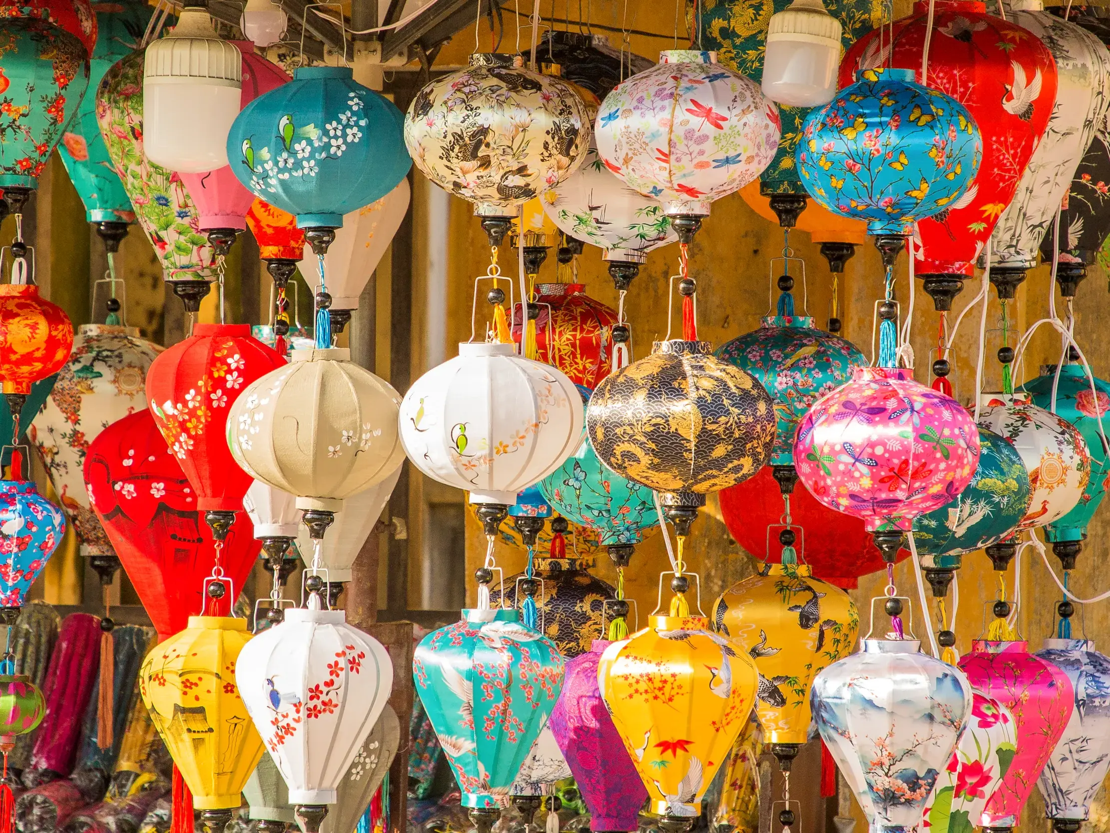 Farbenfrohe, handgefertigte Seidenlampions mit Vogel- und Blumenmotiven hängen dicht gedrängt auf einem Markt in Vietnam.