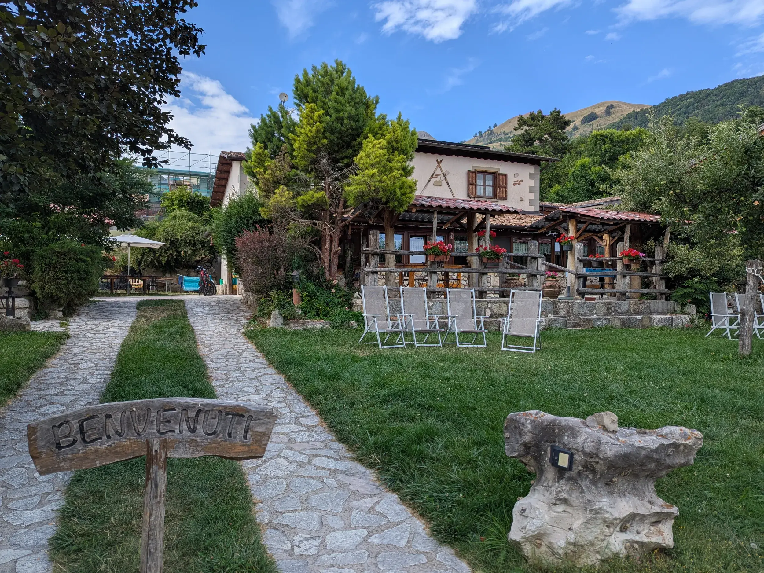 Idyllisches Agriturismo Lu Ceppe mit "Benvenuti"-Schild, grüner Wiese und Liegestühlen vor der Bergkulisse der Apenninen.