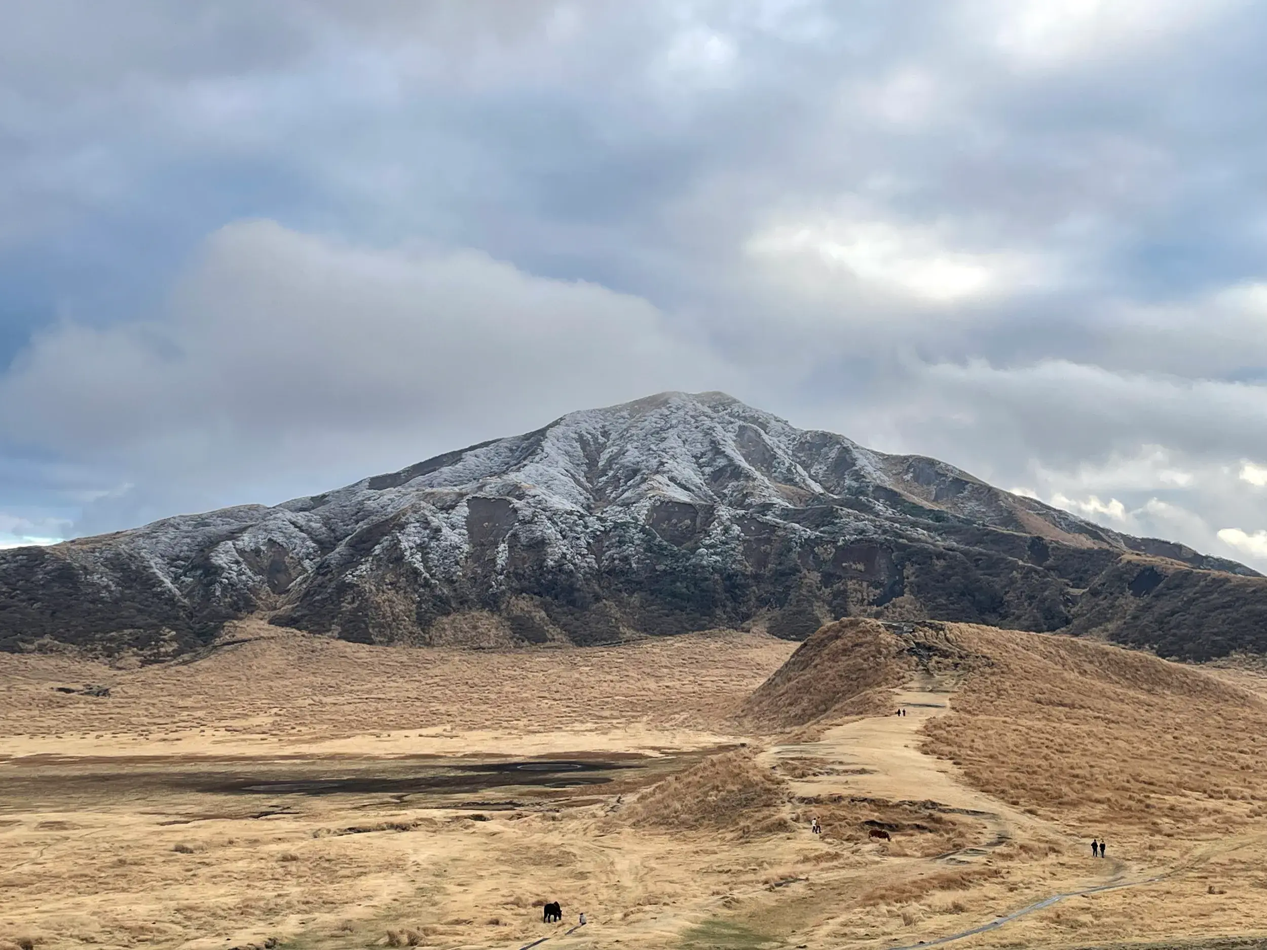 Wanderer in der weiten Caldera des Aso-Kuju-Nationalparks mit Blick auf den schneebedeckten Vulkan Taka-dake in Japan.