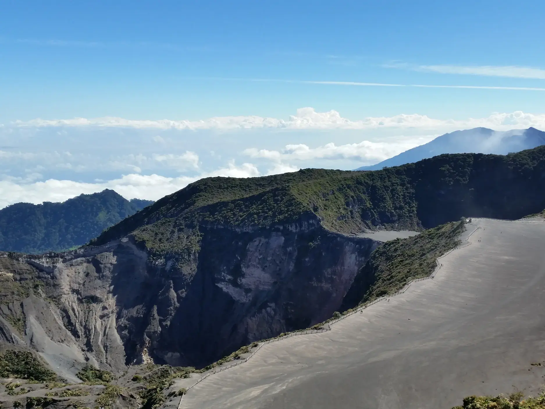 Weitläufige Kraterlandschaft des Vulkans Irazu in Costa Rica mit Wanderern auf einem Pfad am Kraterrand unter blauem Himmel.