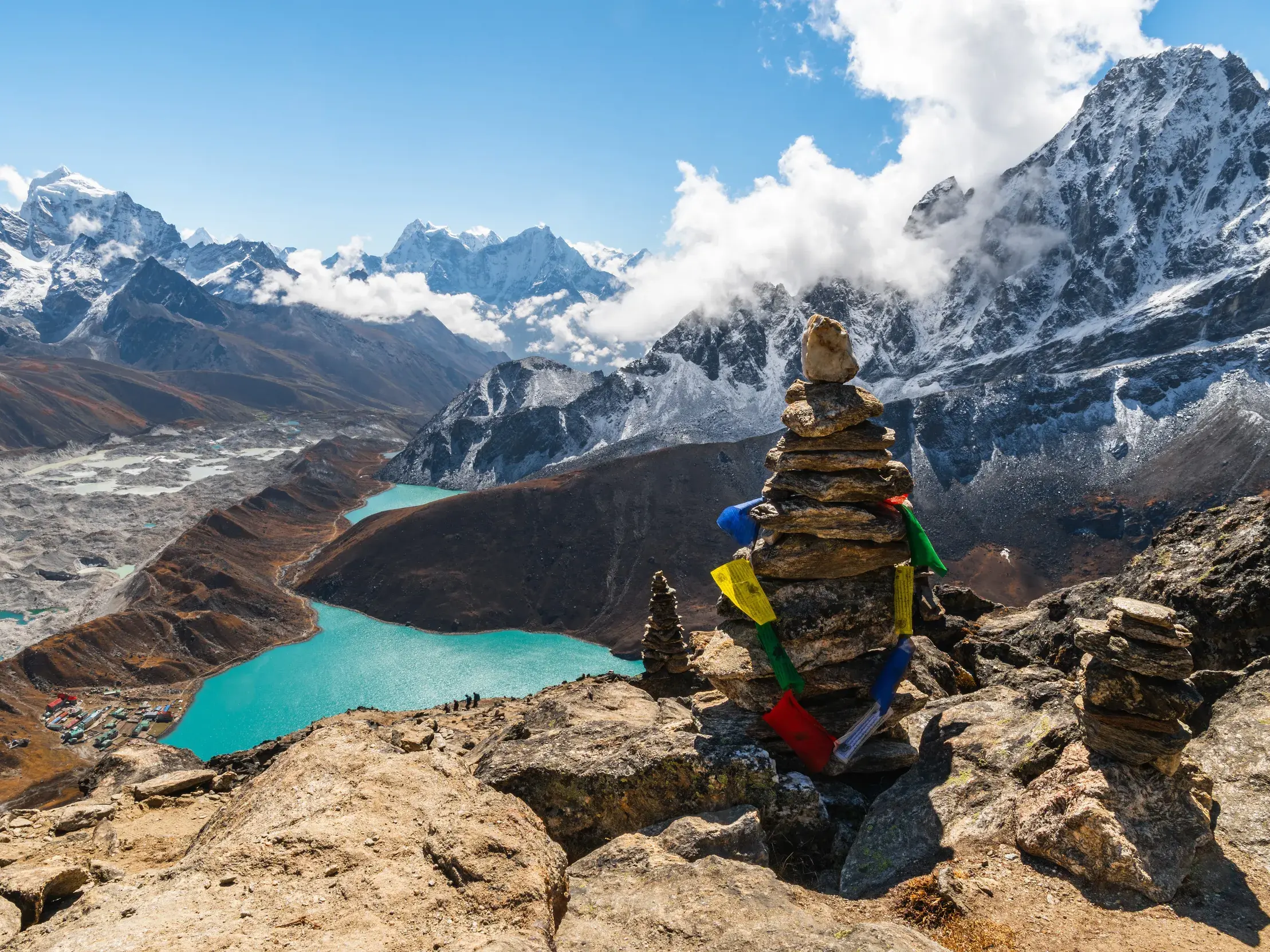 Steinmännchen mit Gebetsfahnen auf dem Gokyo Ri mit Blick auf den türkisen Gokyo-See und das gewaltige Himalaya-Panorama in Nepal.