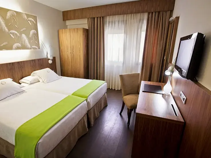 Modernes Zweibettzimmer mit Holzmöbeln, Schreibtisch und Fenster im zentral gelegenen Hotel Opera in Madrid.