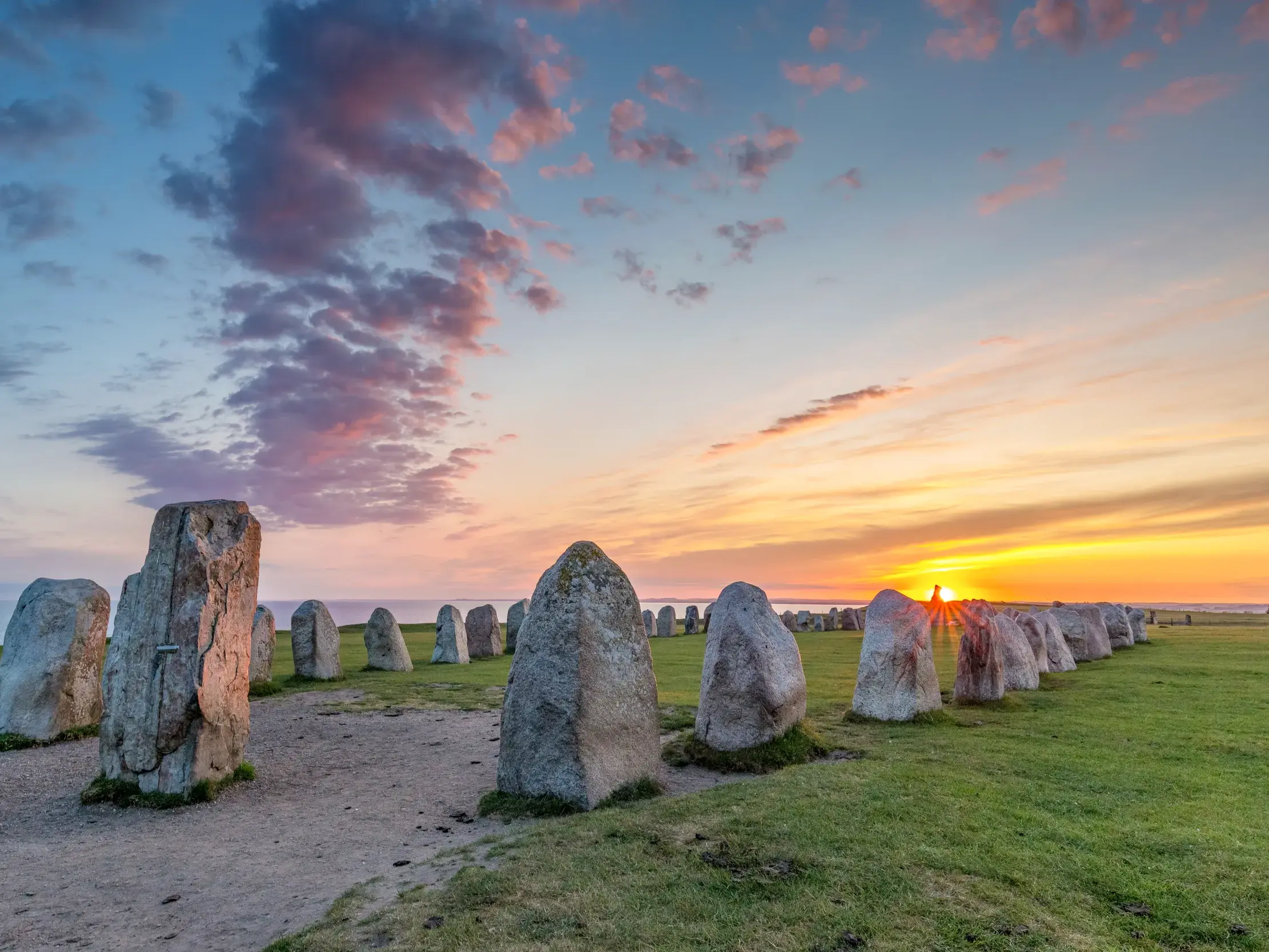 Die mystische Schiffssetzung Ale Stenar in Südschweden auf einer Klippe über dem Meer bei einem farbenprächtigen Sonnenuntergang.