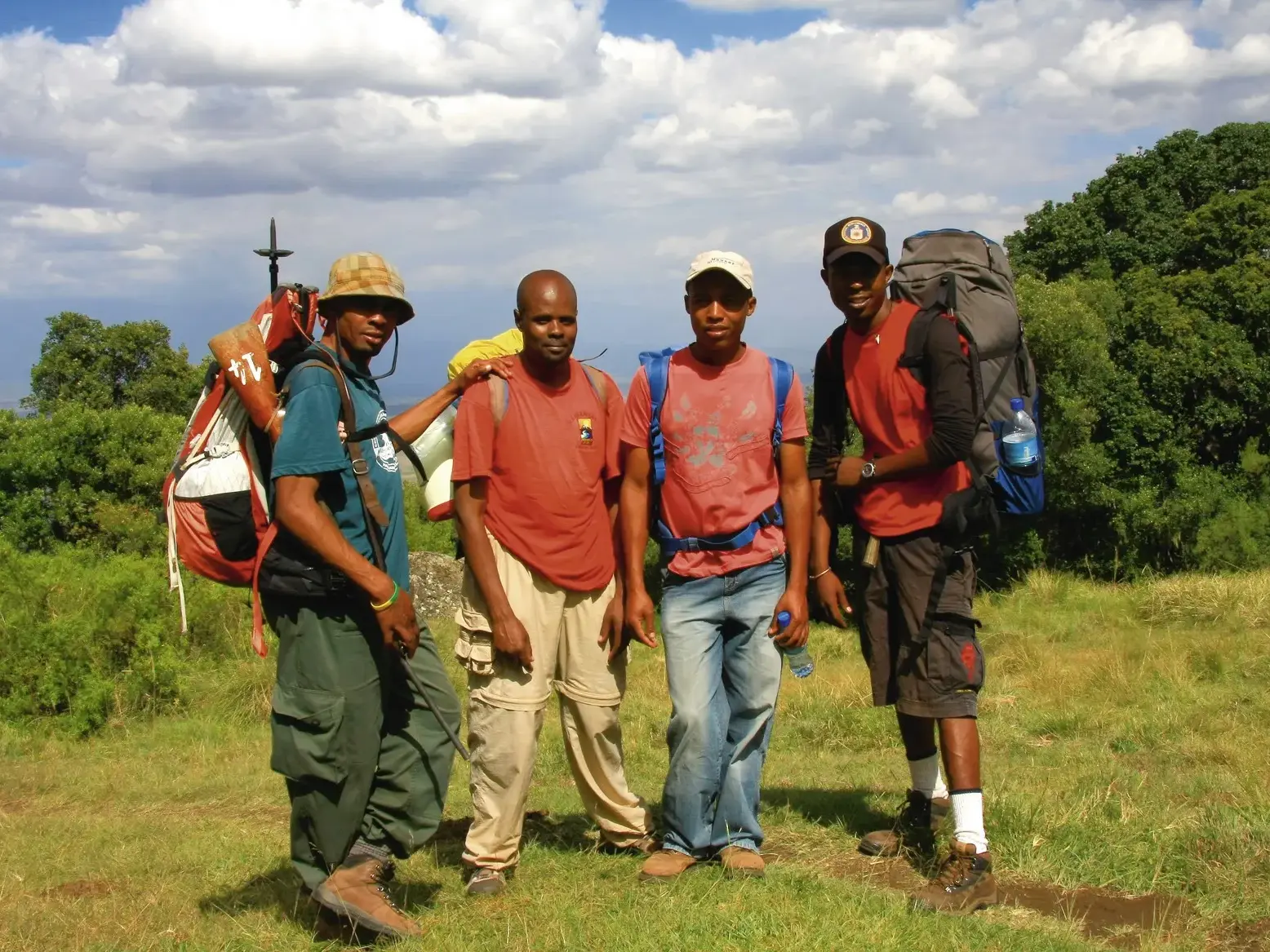 Die freundliche, lokale Begleitmannschaft mit Trekking-Rucksäcken bei einer Pause während der Mount Meru Besteigung in Tansania.