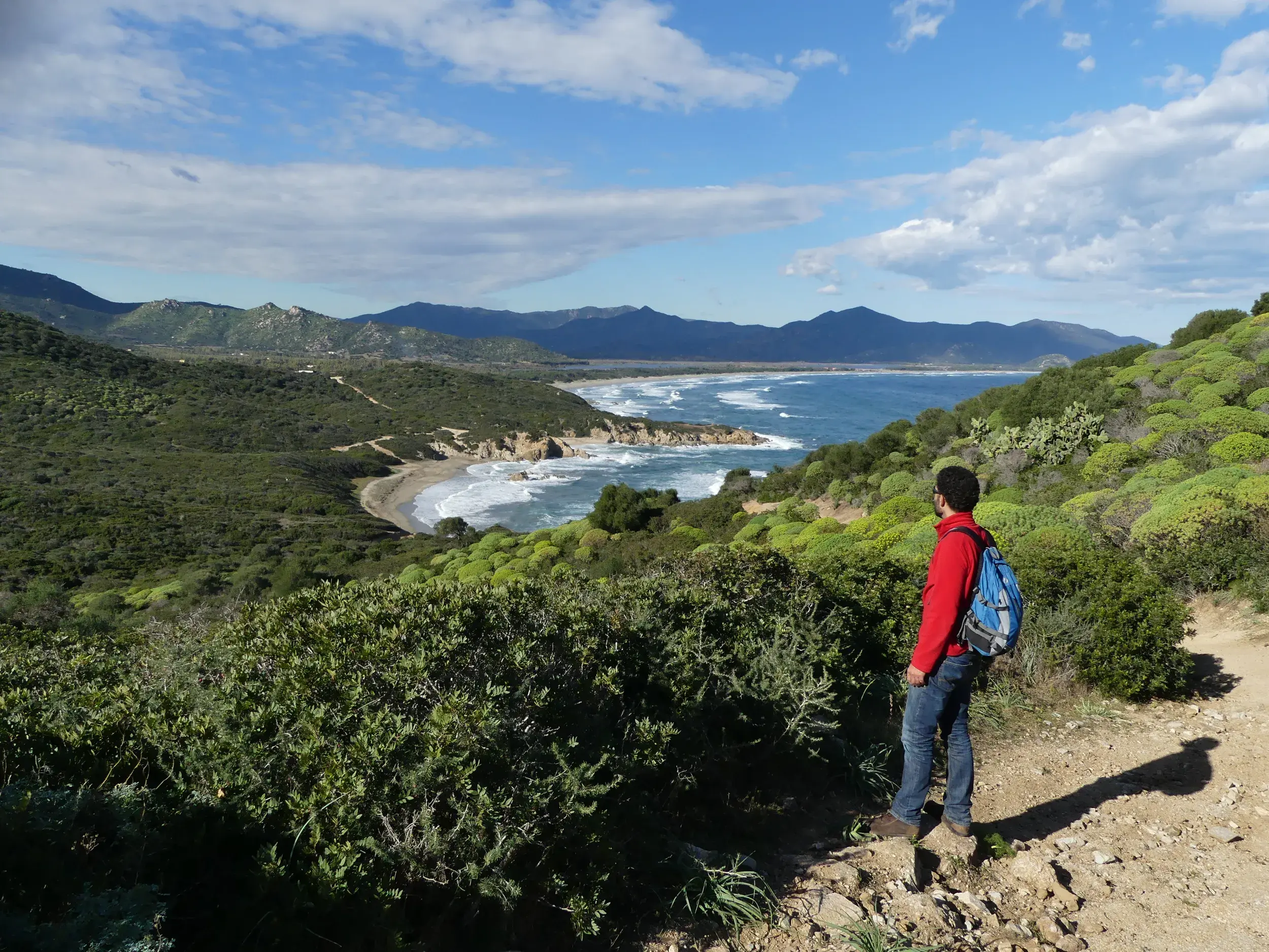Wanderer mit Rucksack genießt auf einer Küstenwanderung am Capo Pecora den Ausblick auf das Meer und die Strände Sardiniens.