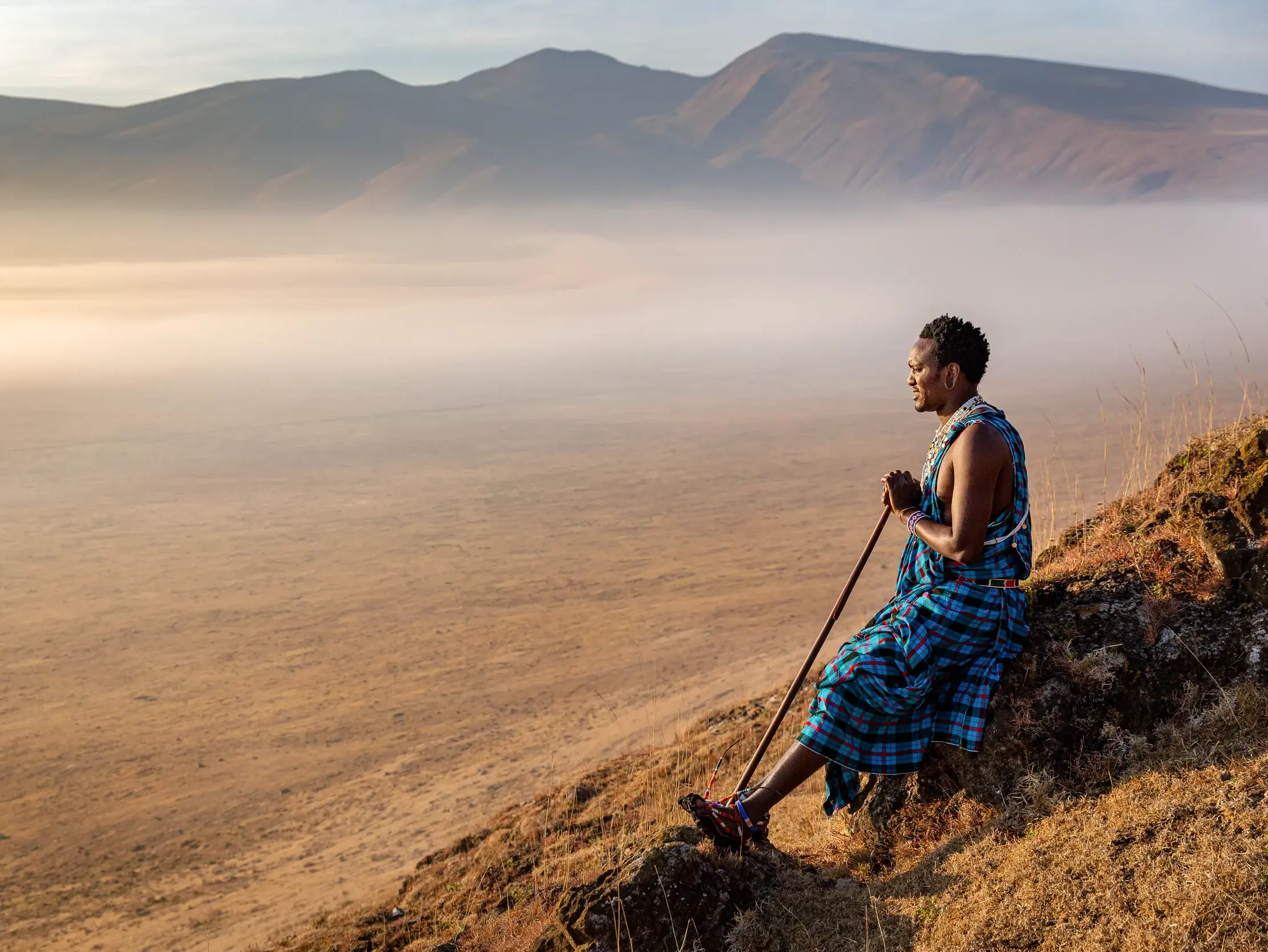 Ein einheimischer Massai-Führer blickt bei Sonnenaufgang über den nebelverhangenen Ngorongoro-Krater in Tansania.