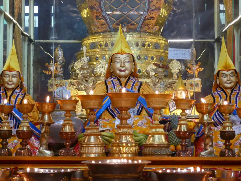 Drei Lama-Statuen mit gelben Hüten in einem Schrein des Jokhang-Tempels in Lhasa, davor leuchten viele Butterlampen.