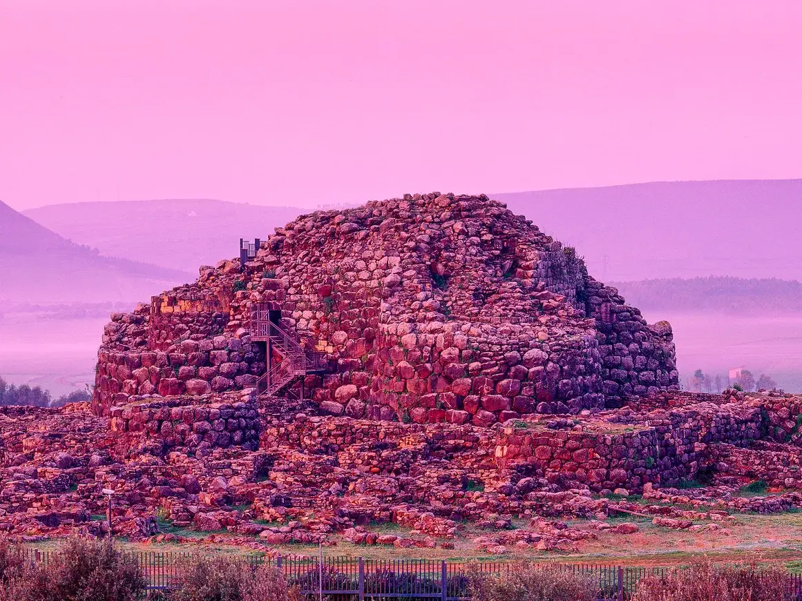 Die prähistorische Festungsanlage Su Nuraxi in Barumini, Sardinien, getaucht in das violette Licht des Sonnenaufgangs.