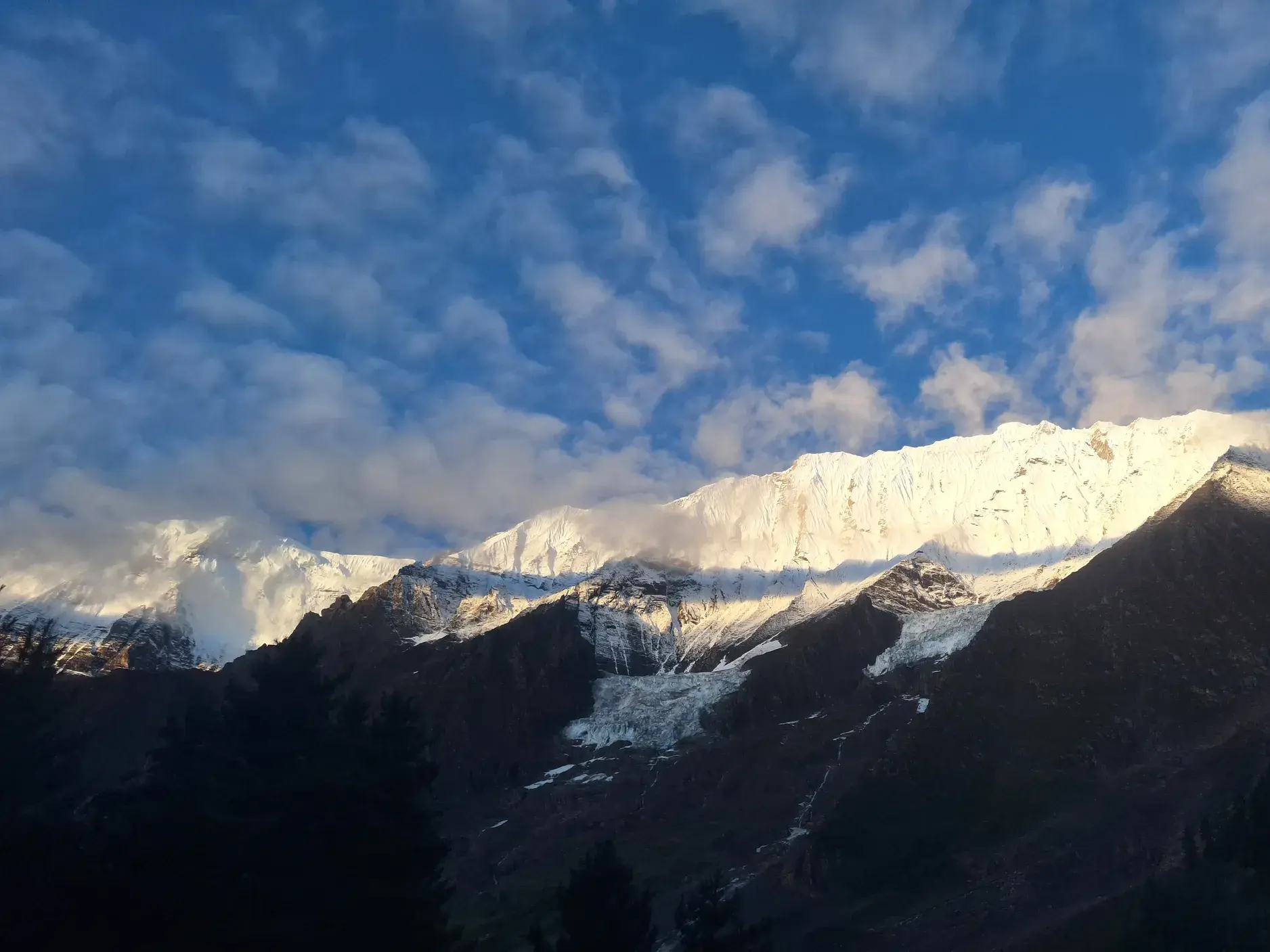 Sonnenschein beleuchtet die schneebedeckten Gipfel der Bergkette im Dolpo, Nepal, unter einem blauen Himmel mit Wolken.