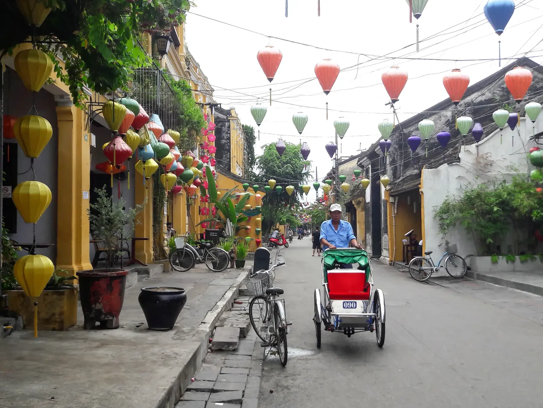 Ein Mann fährt mit einer traditionellen Cyclo-Rikscha durch die mit bunten Lampions dekorierte Altstadt von Hoi An.