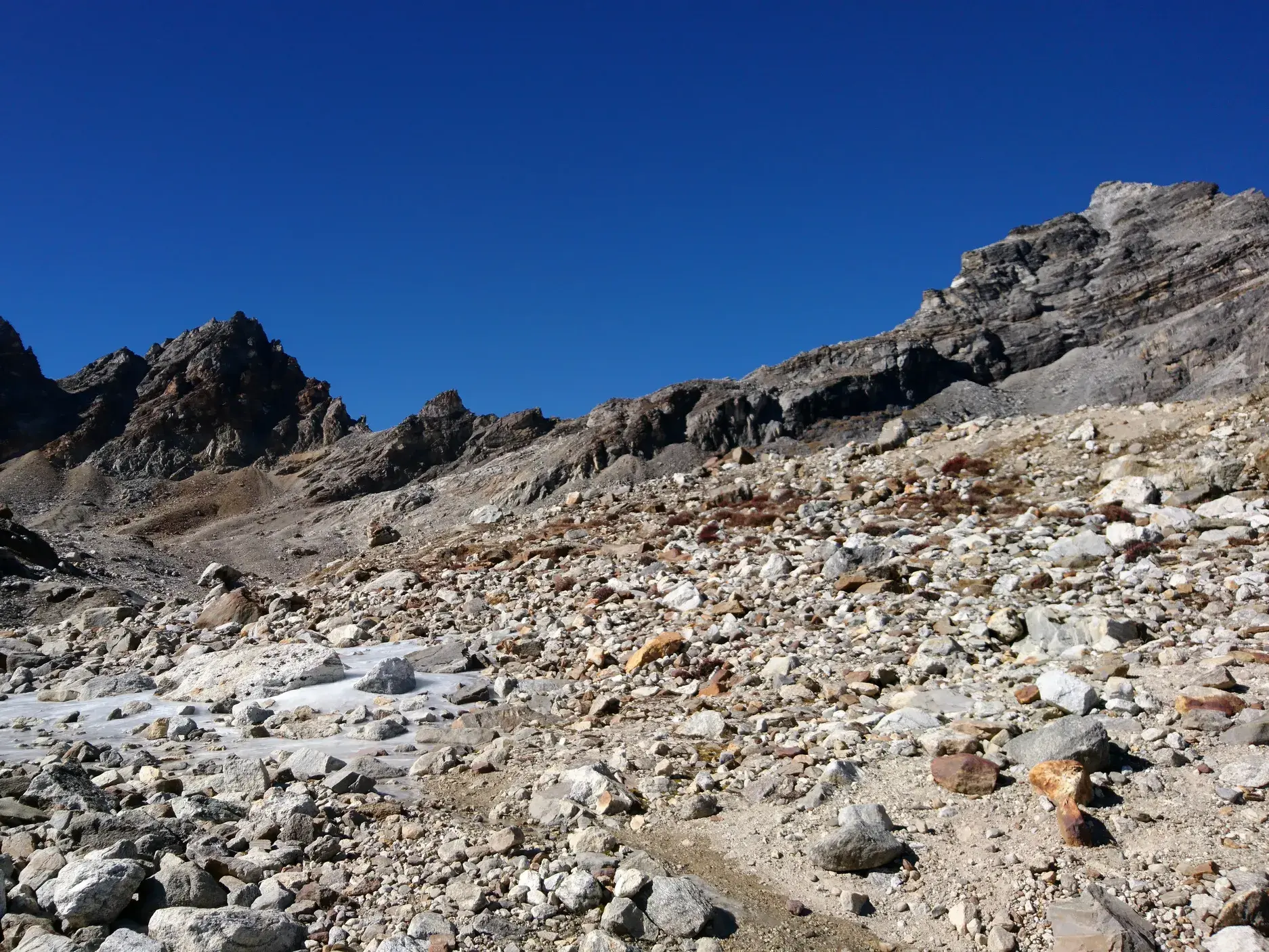 Karge Moränenlandschaft beim Trekking zum Renjo La Pass in Nepal mit schroffen Berggipfeln unter strahlend blauem Himmel.
