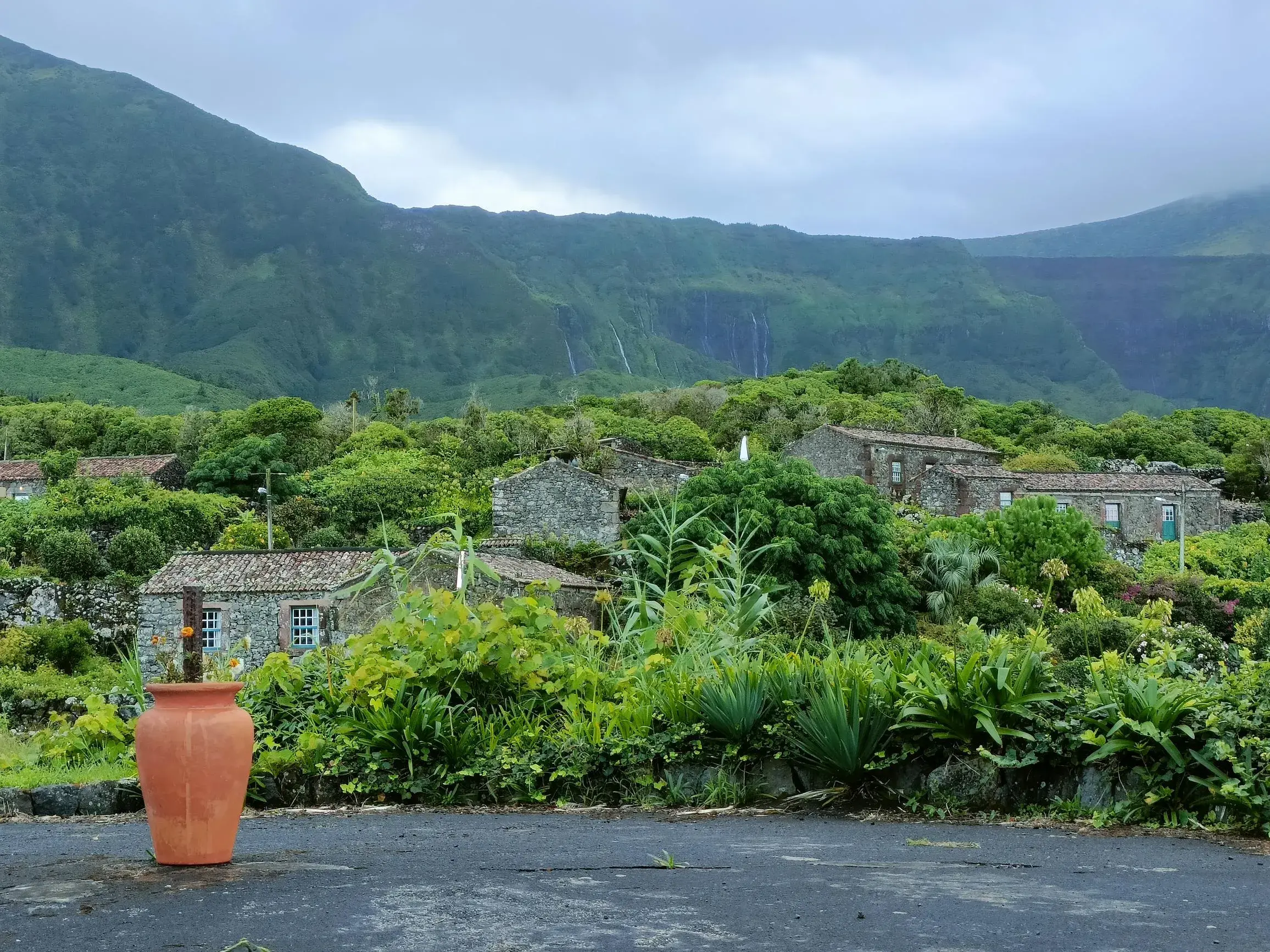 Die traditionelle Unterkunft Aldeia da Cuada auf Flores mit Steinhäusern inmitten grüner Natur und Wasserfällen im Hintergrund.