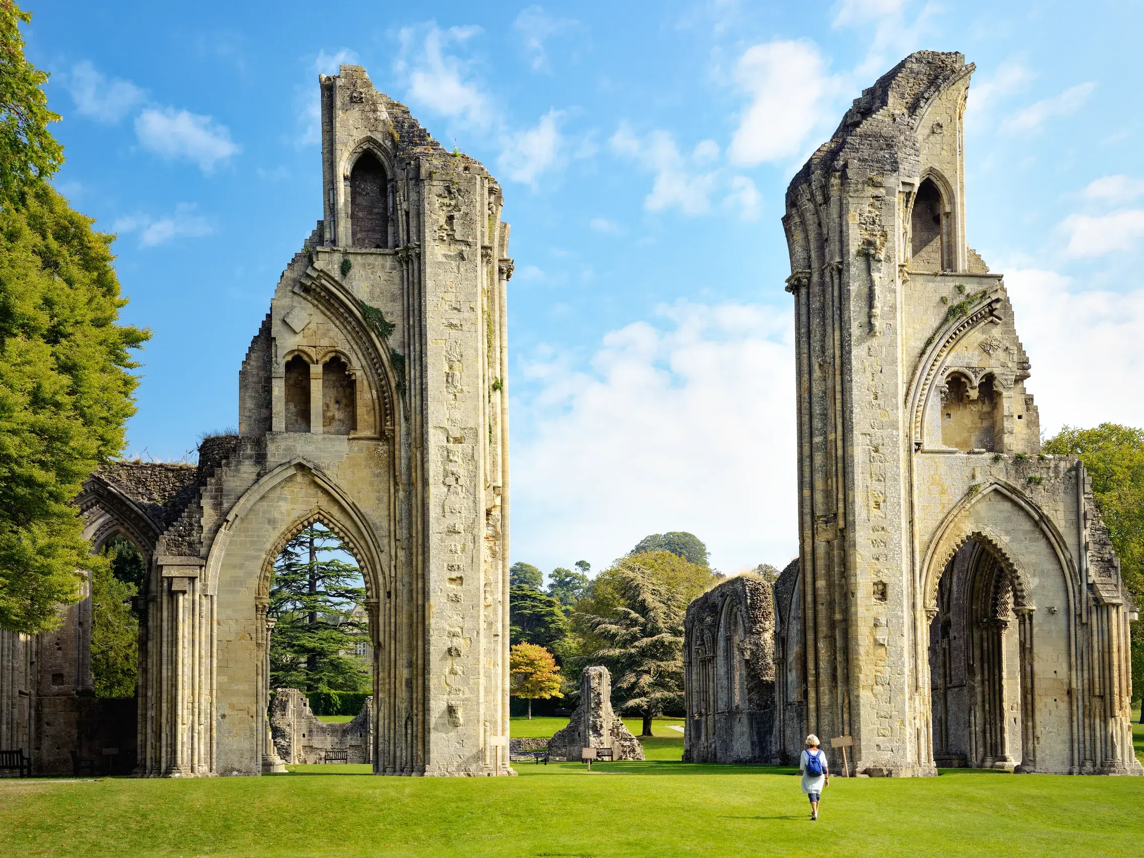 Ein Reisender erkundet die majestätischen Ruinen der Glastonbury Abbey auf einer weitläufigen grünen Wiese in Südengland.