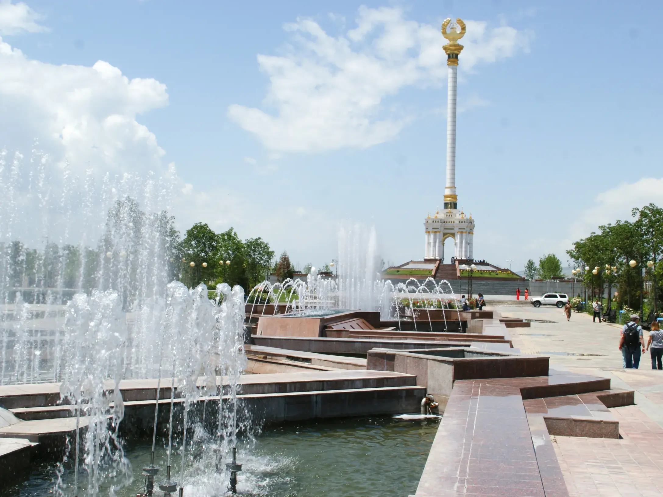 Besucher spazieren an Springbrunnen vorbei zum Unabhängigkeitsdenkmal auf dem weitläufigen Rudaki-Boulevard in Duschanbe.