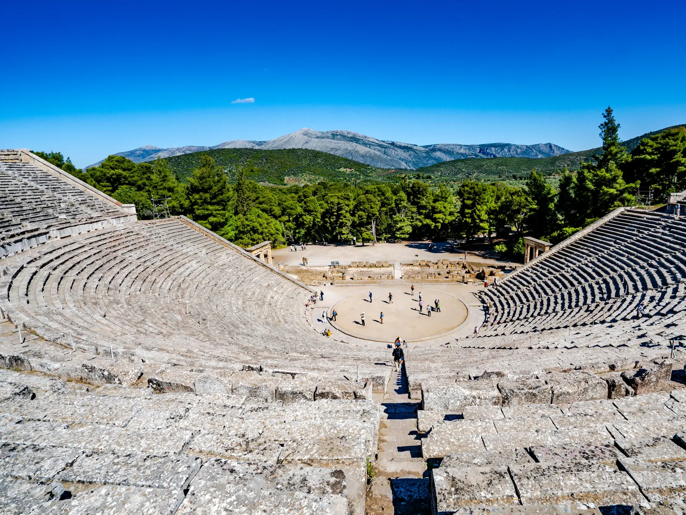 Das gut erhaltene antike Theater von Epidauros an einem sonnigen Tag, im Hintergrund die grüne Landschaft des Peloponnes.