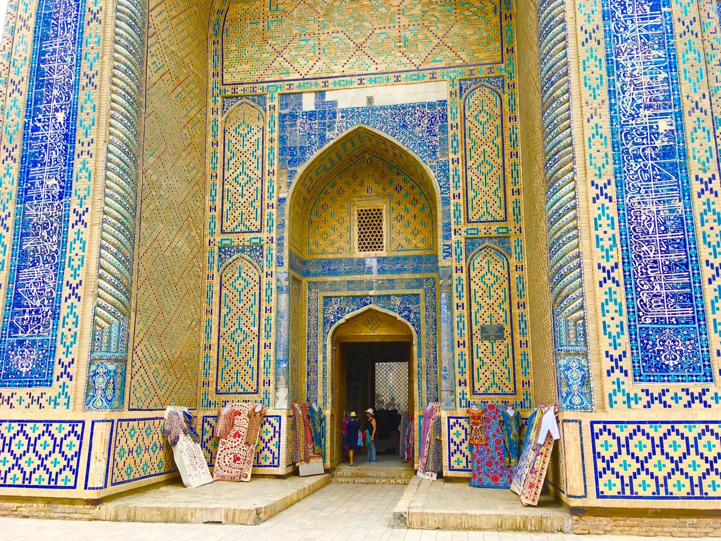 Prunkvoller Eingang eines Mausoleums in Shohizinda, Samarkand, mit blauen Mosaikfliesen und zum Verkauf stehenden Teppichen.