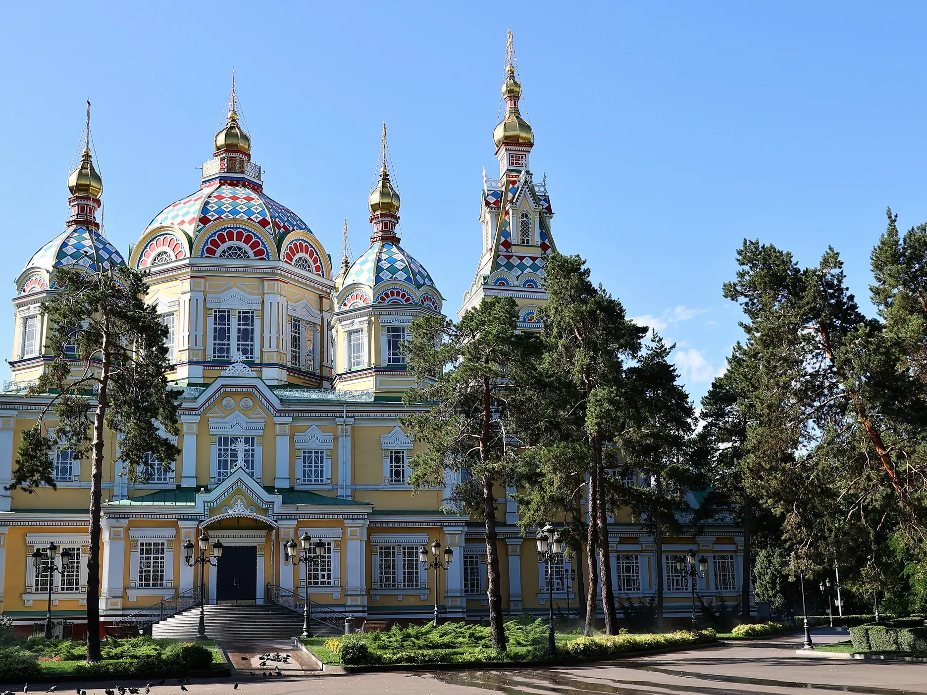 Die farbenprächtige Christi-Himmelfahrt-Kathedrale mit goldenen Zwiebeltürmen in Almaty, umgeben von Bäumen im Panfilov Park.