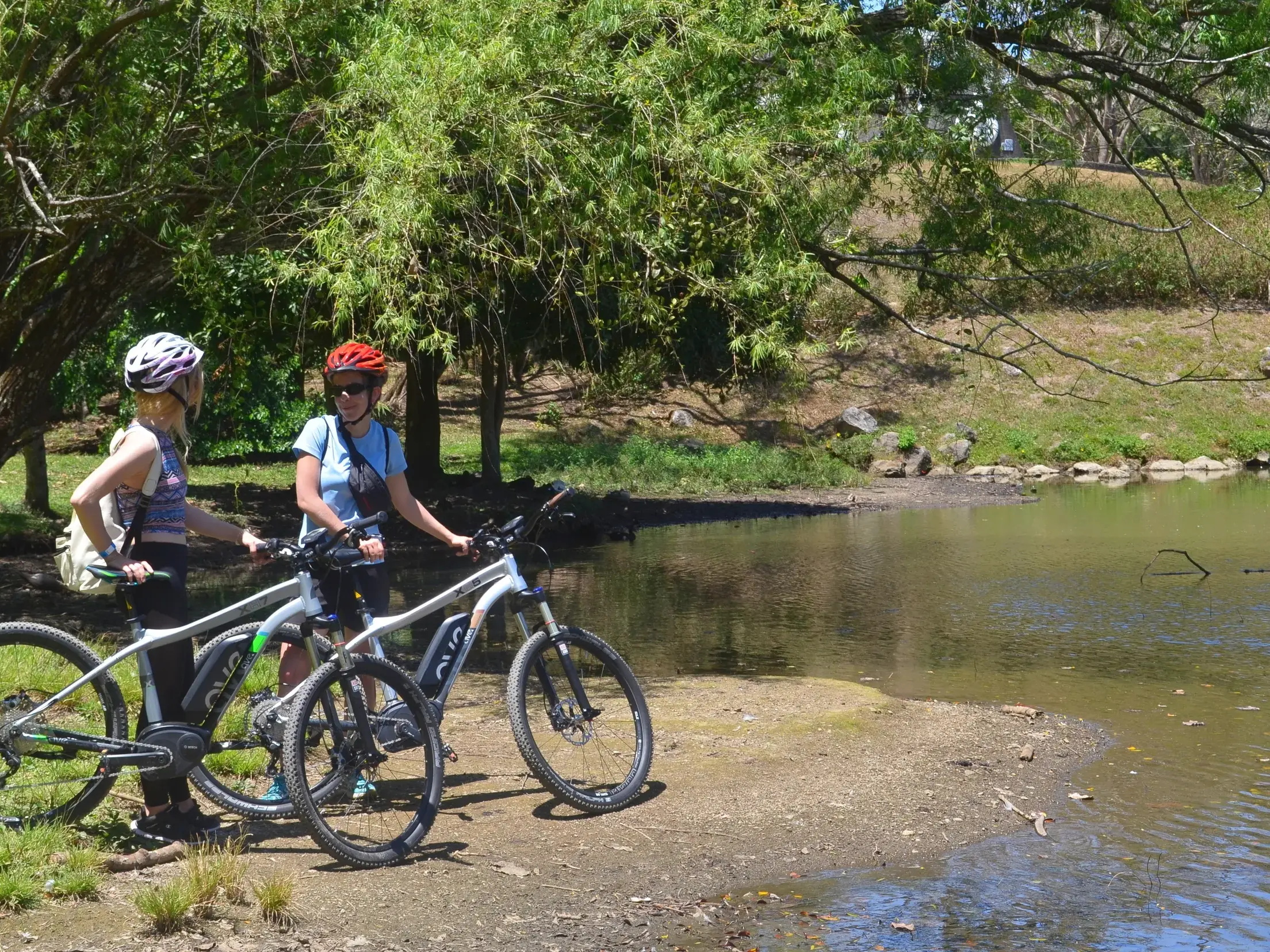 Zwei Radfahrerinnen mit E-Mountainbikes machen während ihrer geführten Radreise in Costa Rica eine Pause am Ufer eines Sees.