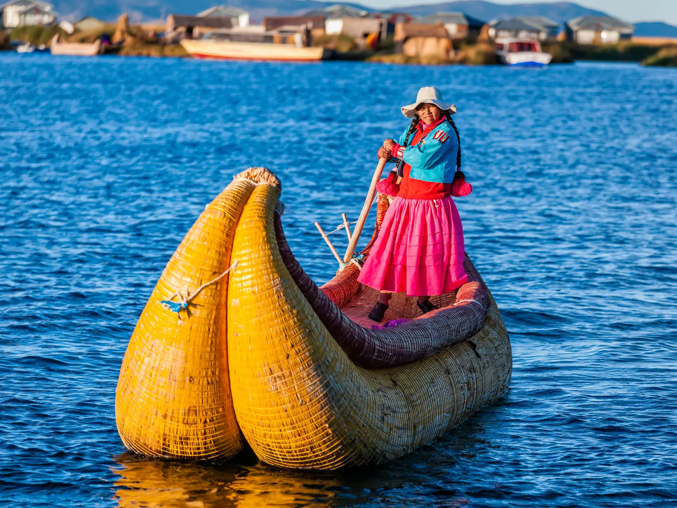 Eine lächelnde Uros-Frau in traditioneller Tracht steuert ihr gelbes Totora-Schilfboot über den blauen Titicacasee in Peru.