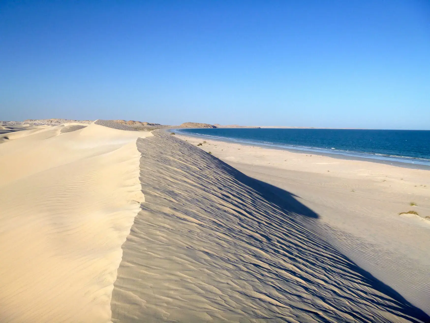 Eine hohe, weiße Sanddüne mit Windverwehungen an der Küste des Indischen Ozeans in der Wüste Al Khaluf im Oman.