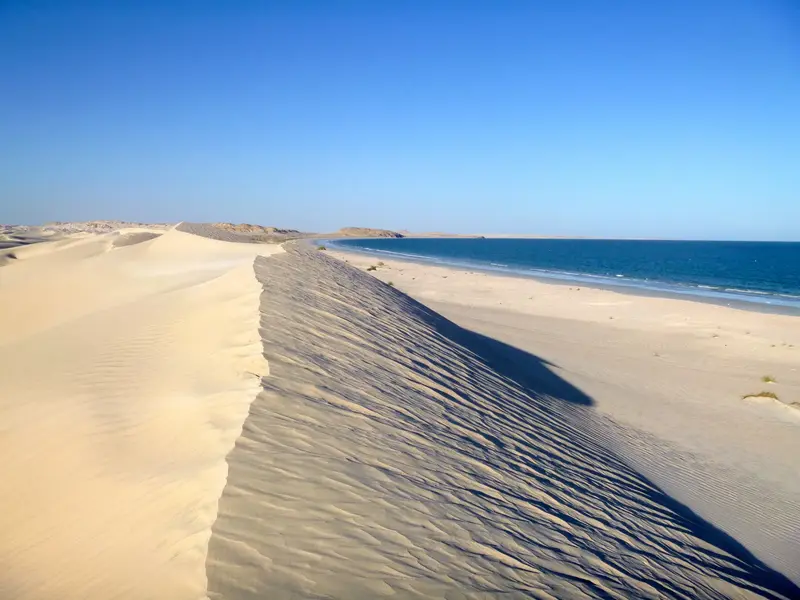 Eine hohe, weiße Sanddüne mit Windverwehungen an der Küste des Indischen Ozeans in der Wüste Al Khaluf im Oman.