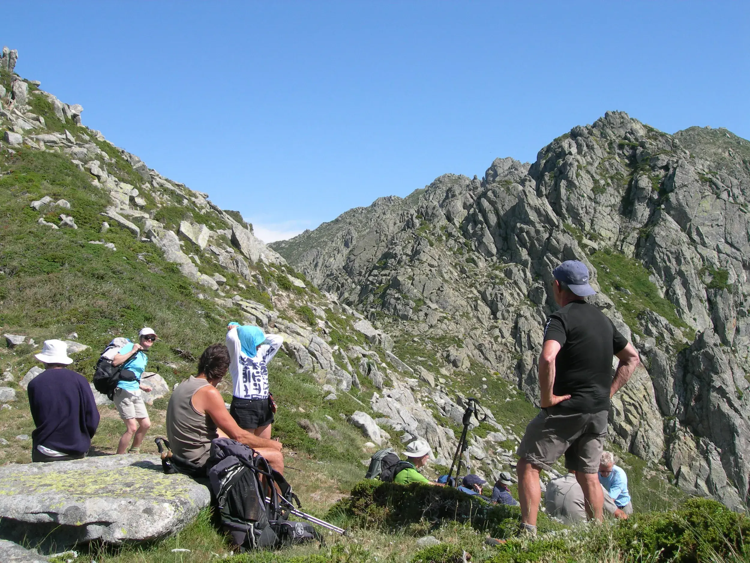 Eine Wandergruppe legt beim Trekking auf dem GR20 eine Rast ein und genießt den Ausblick auf die schroffen Berge Korsikas.