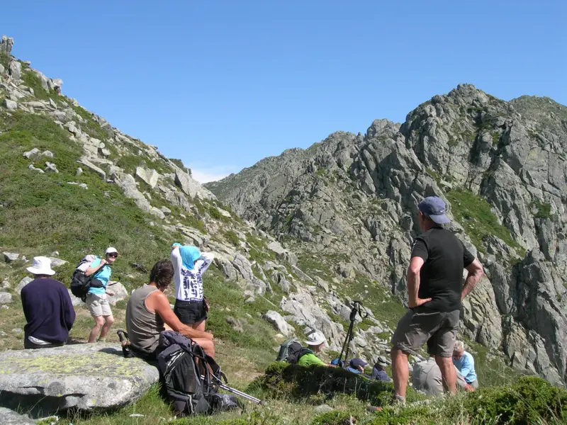 Eine Wandergruppe legt beim Trekking auf dem GR20 eine Rast ein und genießt den Ausblick auf die schroffen Berge Korsikas.