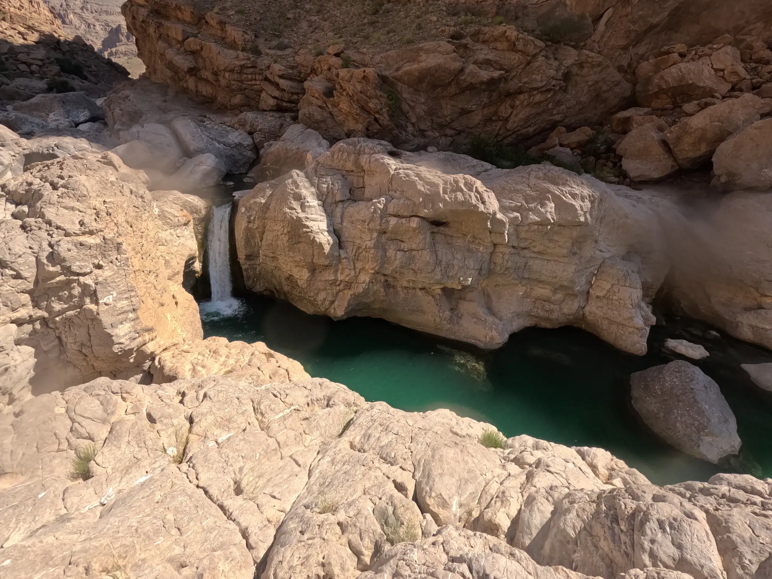 Kleiner Wasserfall stürzt in ein türkisfarbenes Wasserbecken bei einer Wanderung durch die Felsschlucht des Wadi Tiwi im Oman.