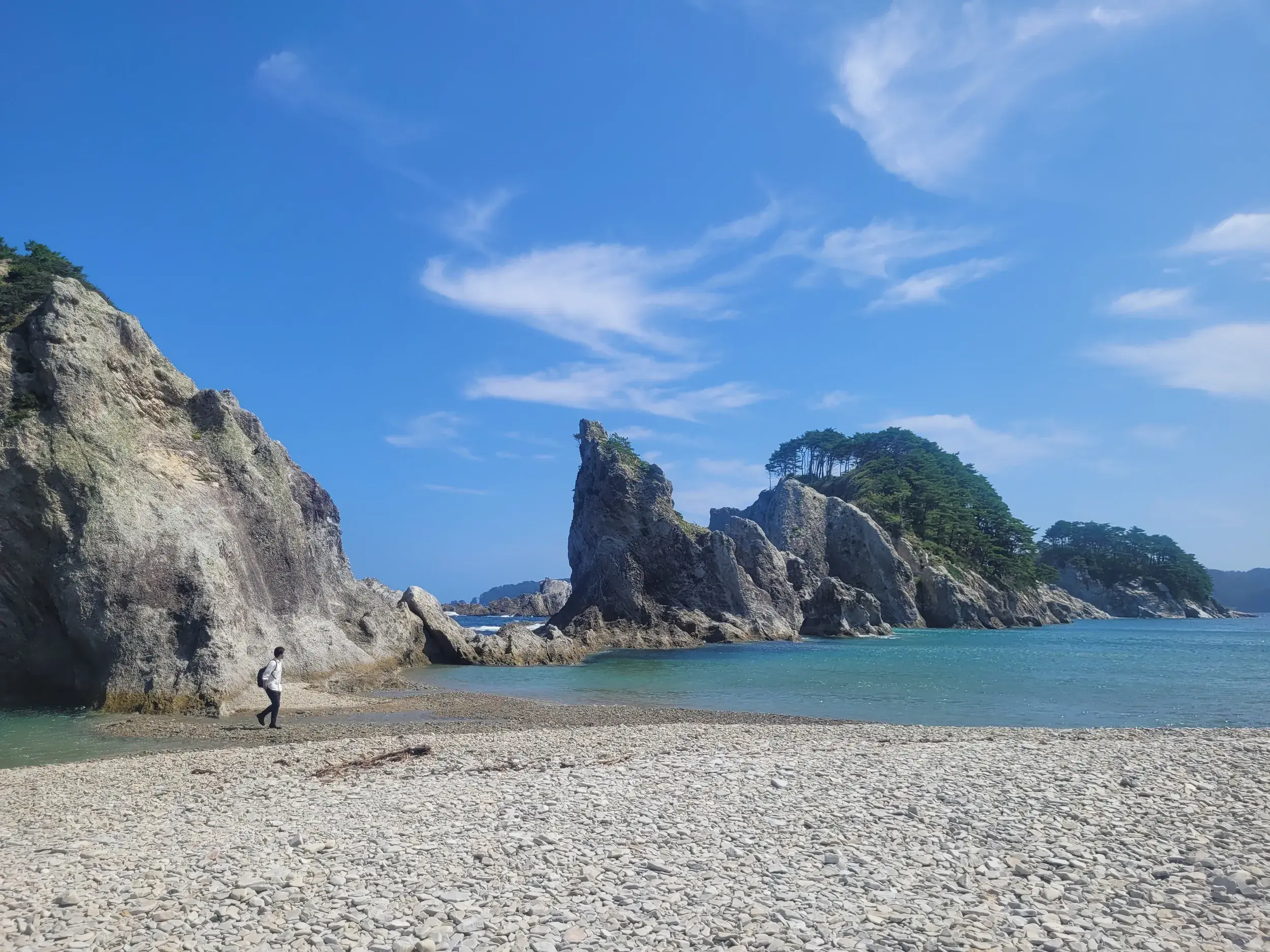 Ein Wanderer erkundet die wilde Felsküste Japans auf einem Kiesstrand am malerischen Michinoku Coastal Trail.