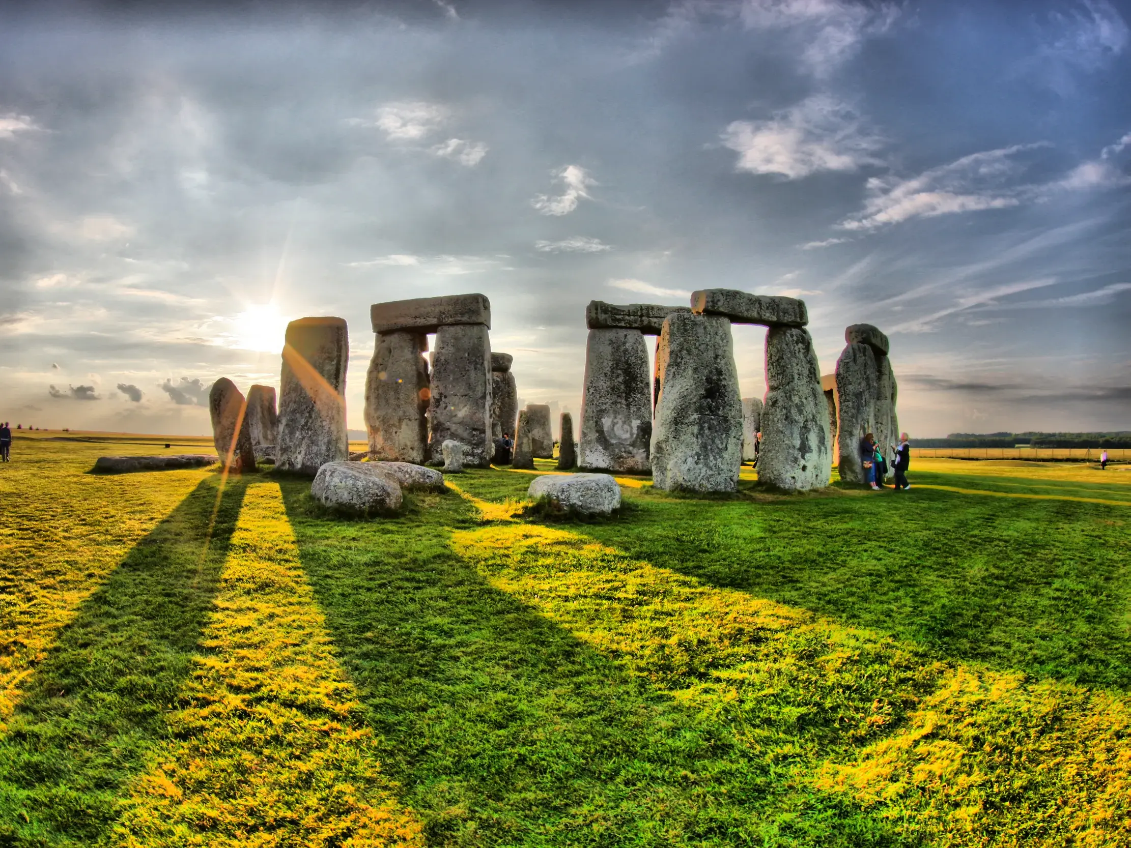 Das UNESCO-Welterbe Stonehenge bei Sonnenuntergang. Die Steine werfen lange Schatten auf die grüne Wiese in Südengland.