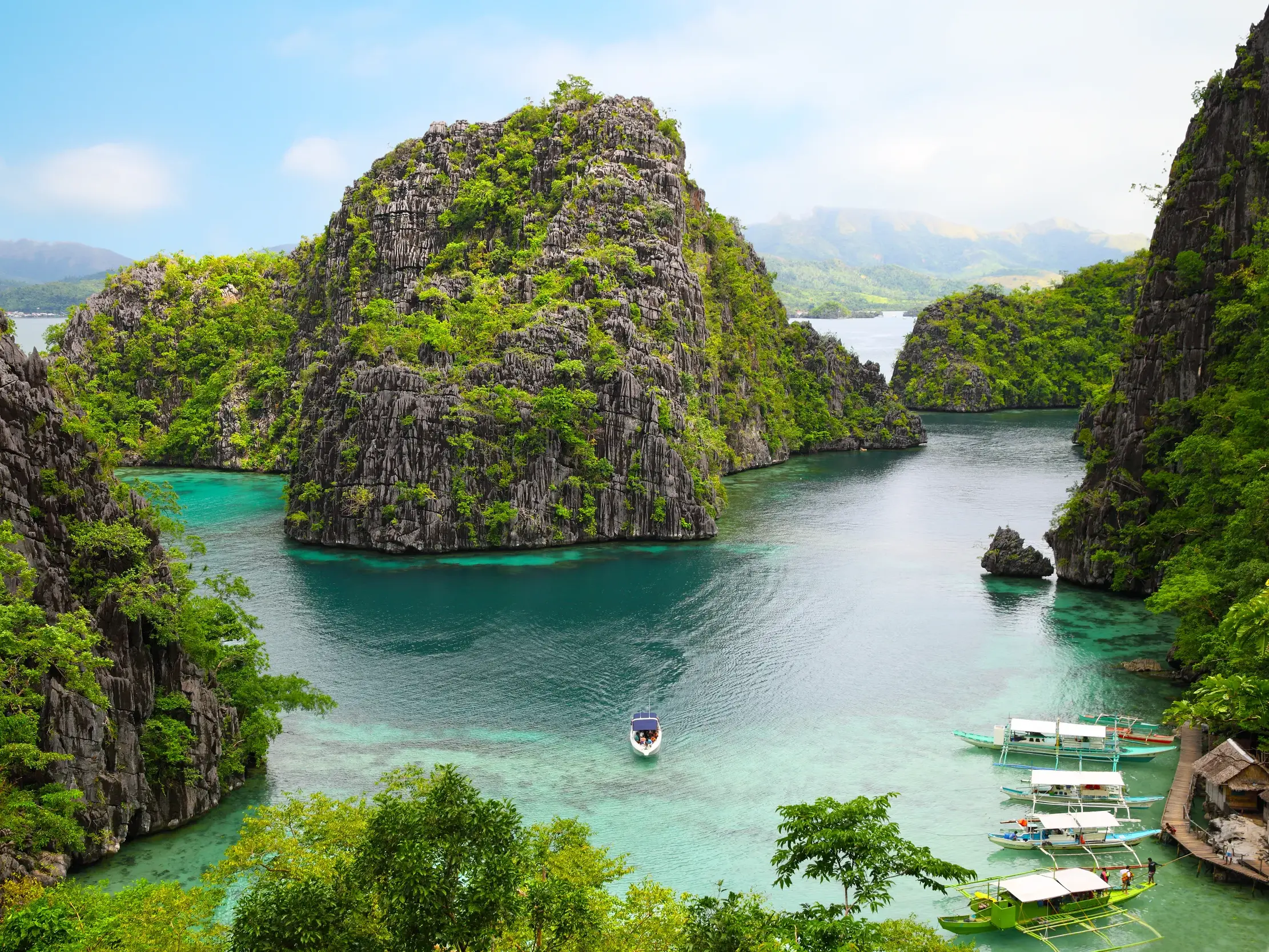 Erhöhter Ausblick auf eine türkisfarbene Lagune auf Coron, umgeben von grünen Karstfelsen und traditionellen Banca-Booten.