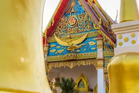 Nahaufnahme des prächtig verzierten Giebels eines Tempels in Thailand mit einer goldenen Garuda-Figur vor blauem Mosaik.