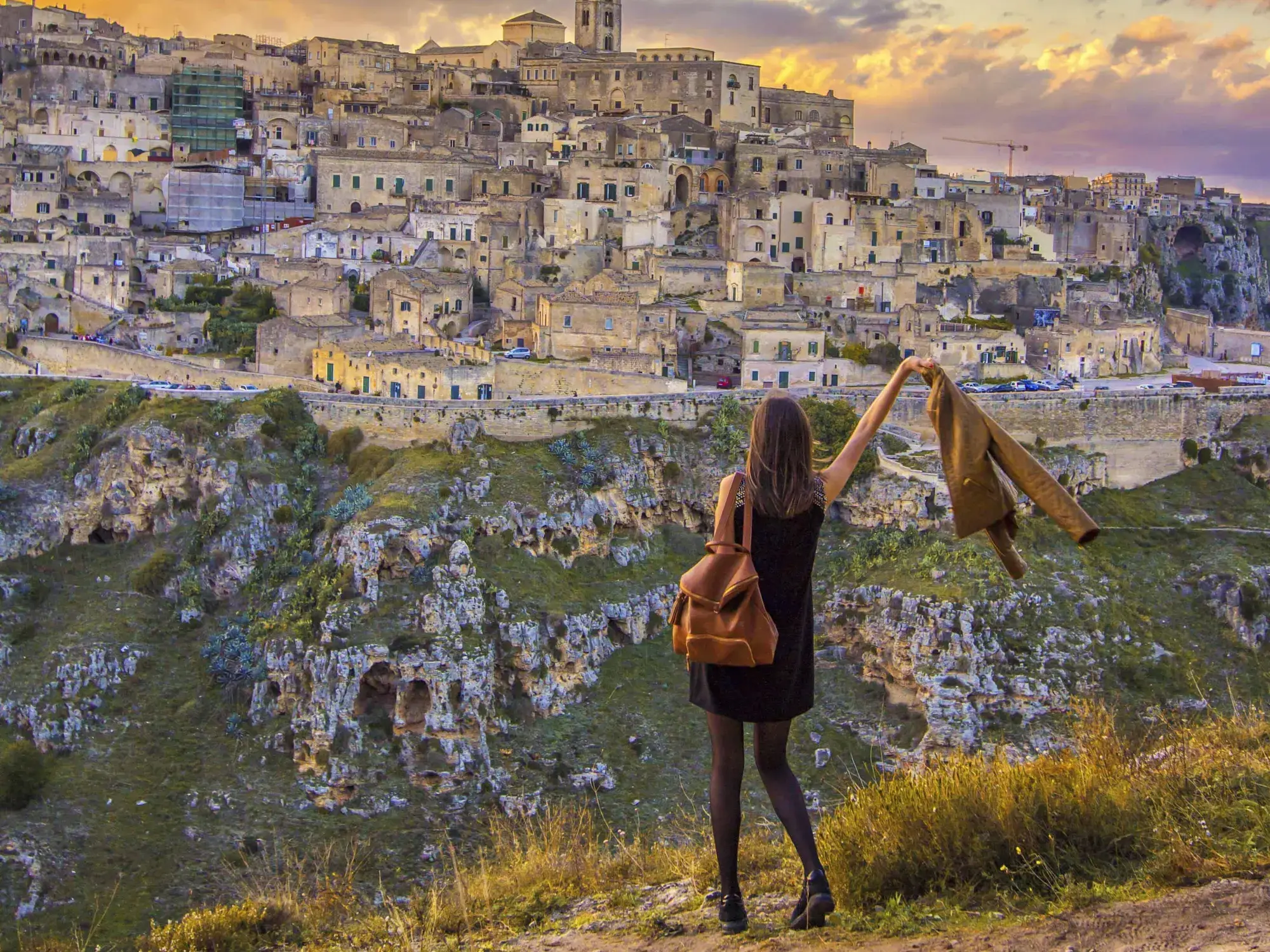 Eine Alleinreisende genießt den Panoramablick auf die historische Felsenstadt Matera in der Basilikata bei Sonnenuntergang.